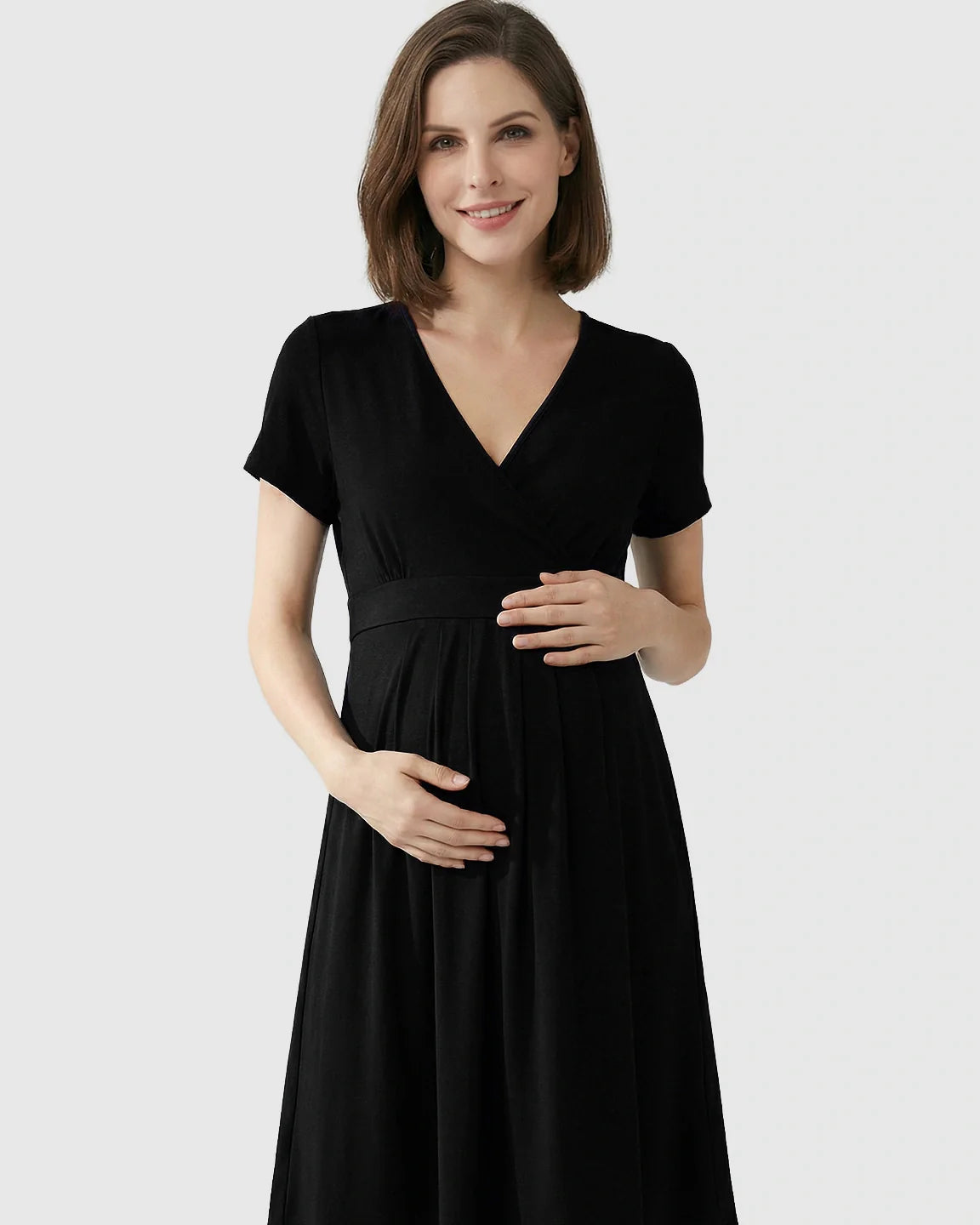 Smiling pregnant woman in a black V-neck A-line maternity and nursing dress, holding her bump.