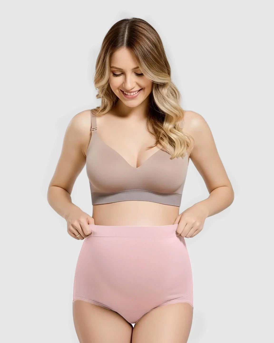 Smiling pregnant woman in a beige bra and pink seamless high-waist maternity panties.