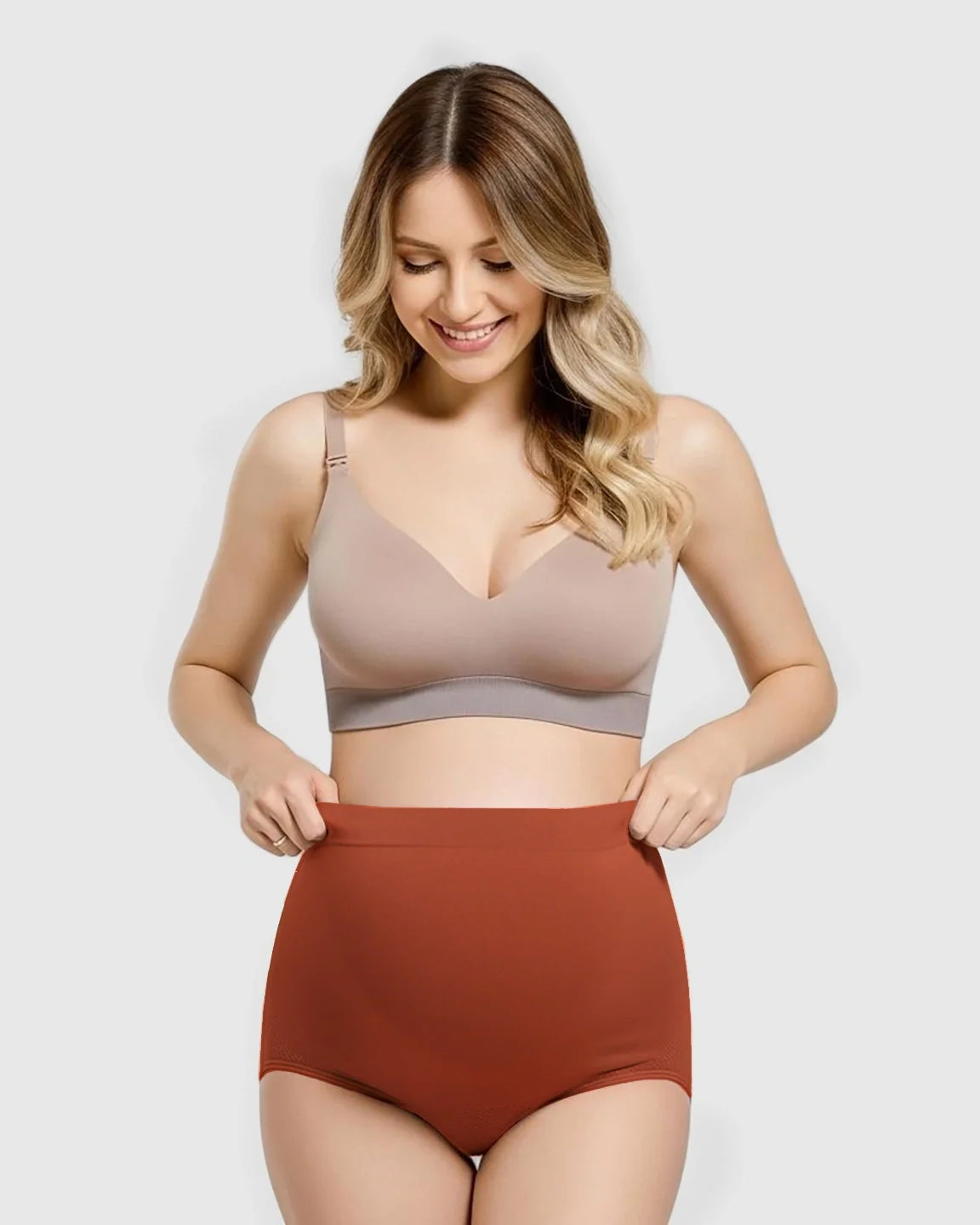 Smiling pregnant woman in a beige bra and rust-colored seamless high-waist maternity panties.