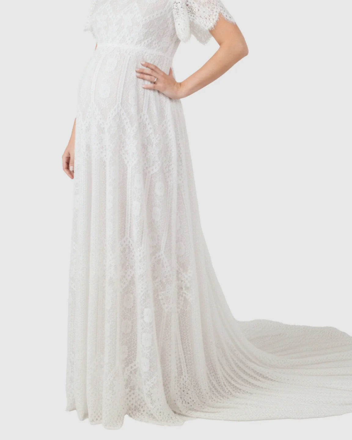 White vintage lace flutter-sleeve maternity gown with a long trailing hem, highlighting a pregnant belly.