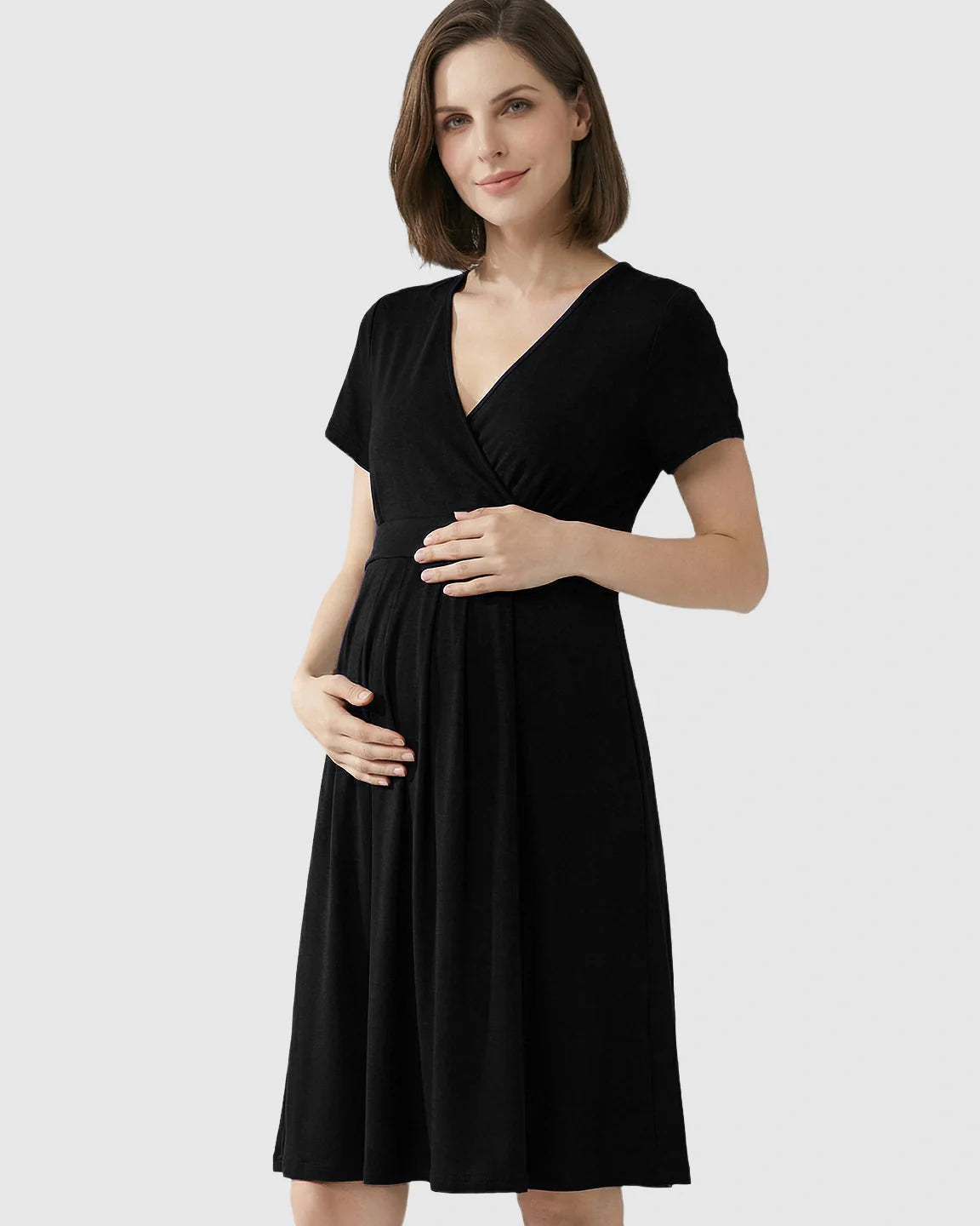 Woman in a black V-neck A-line maternity and nursing dress, holding her baby bump.