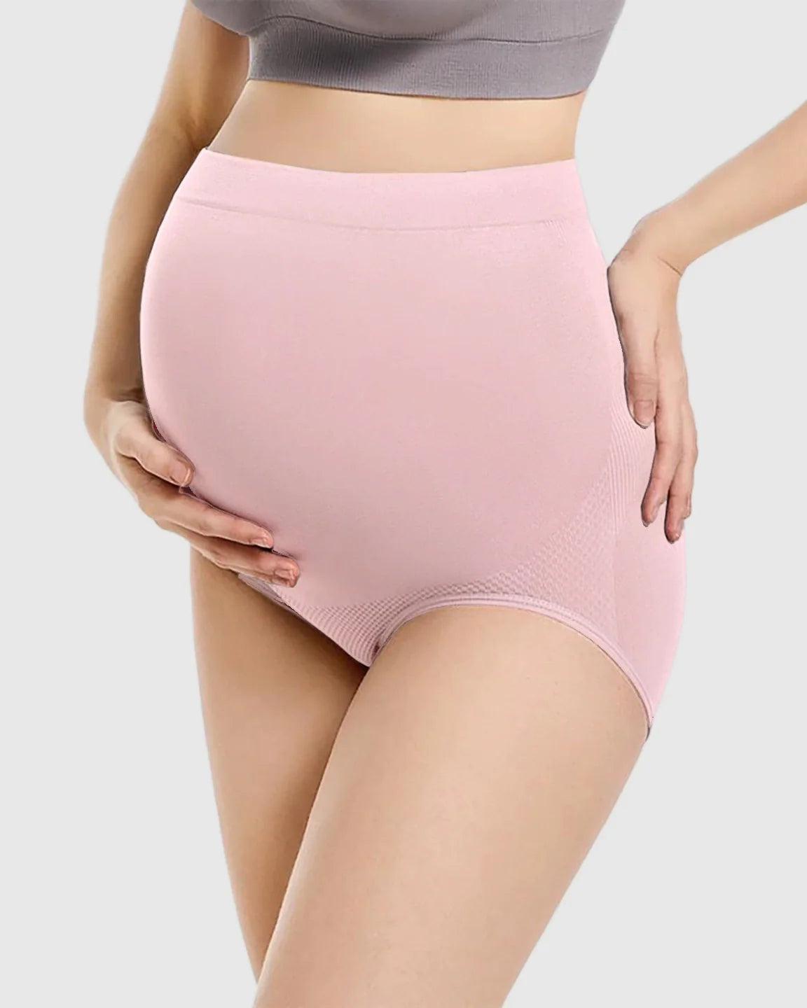 Pregnant woman wearing pink high-waist seamless maternity panties, supporting her bump.