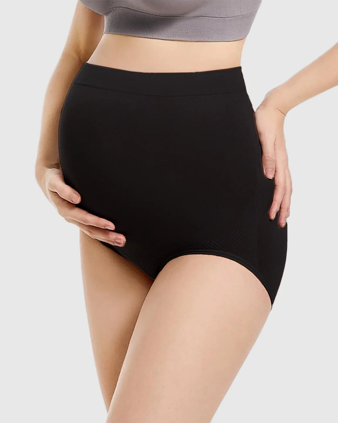 Black seamless high-waist maternity panties on a pregnant model, supporting the bump.