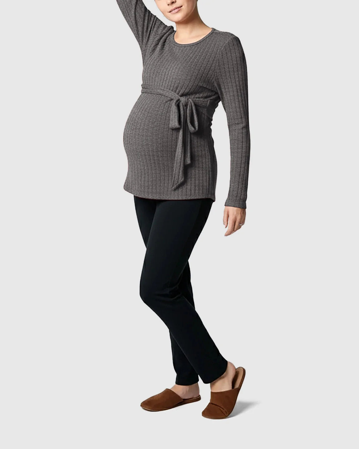 Maternity model in a gray ribbed tie-waist long sleeve sweater, black pants, and brown slippers.