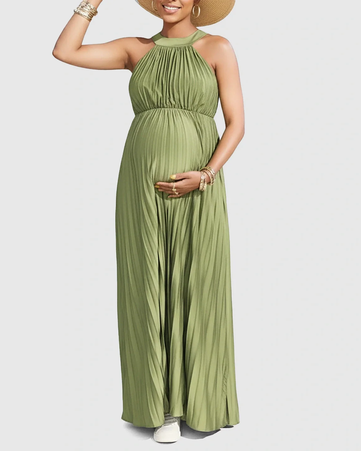 Maternity model in a green faux silk halter neck pleated maxi dress, wearing a straw hat and gold bracelets.