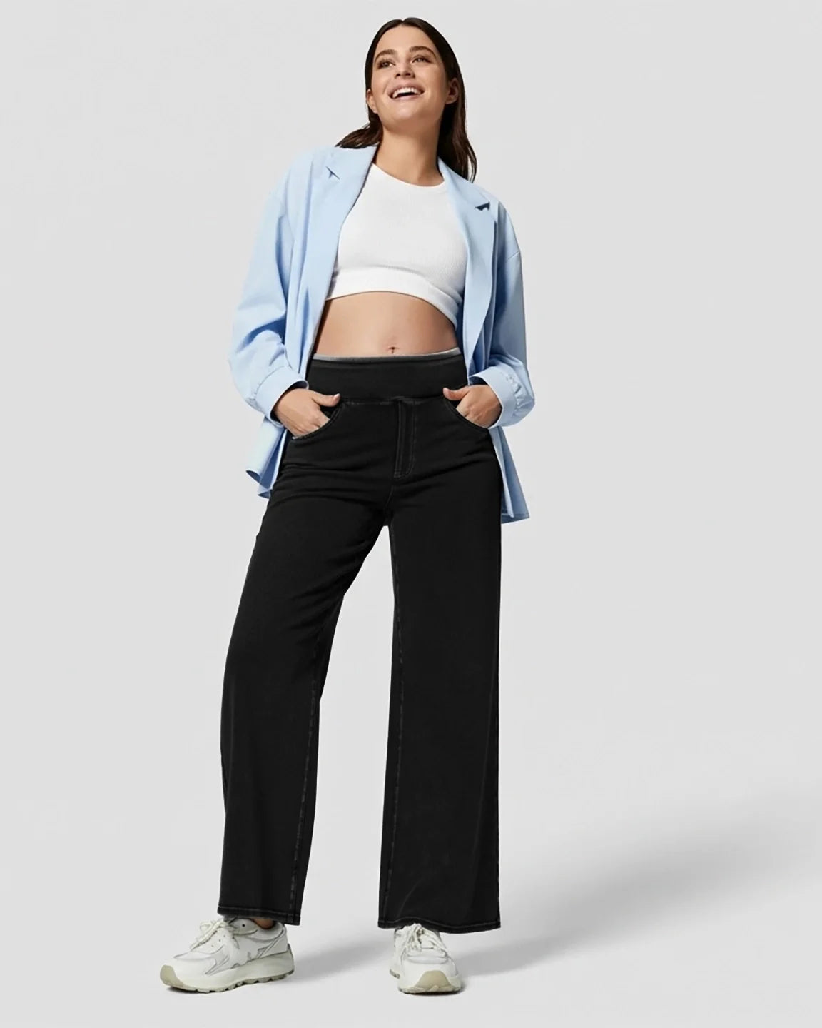 Smiling pregnant woman in black high-waist wide-leg maternity denim jeans, white crop top, and blue blazer.