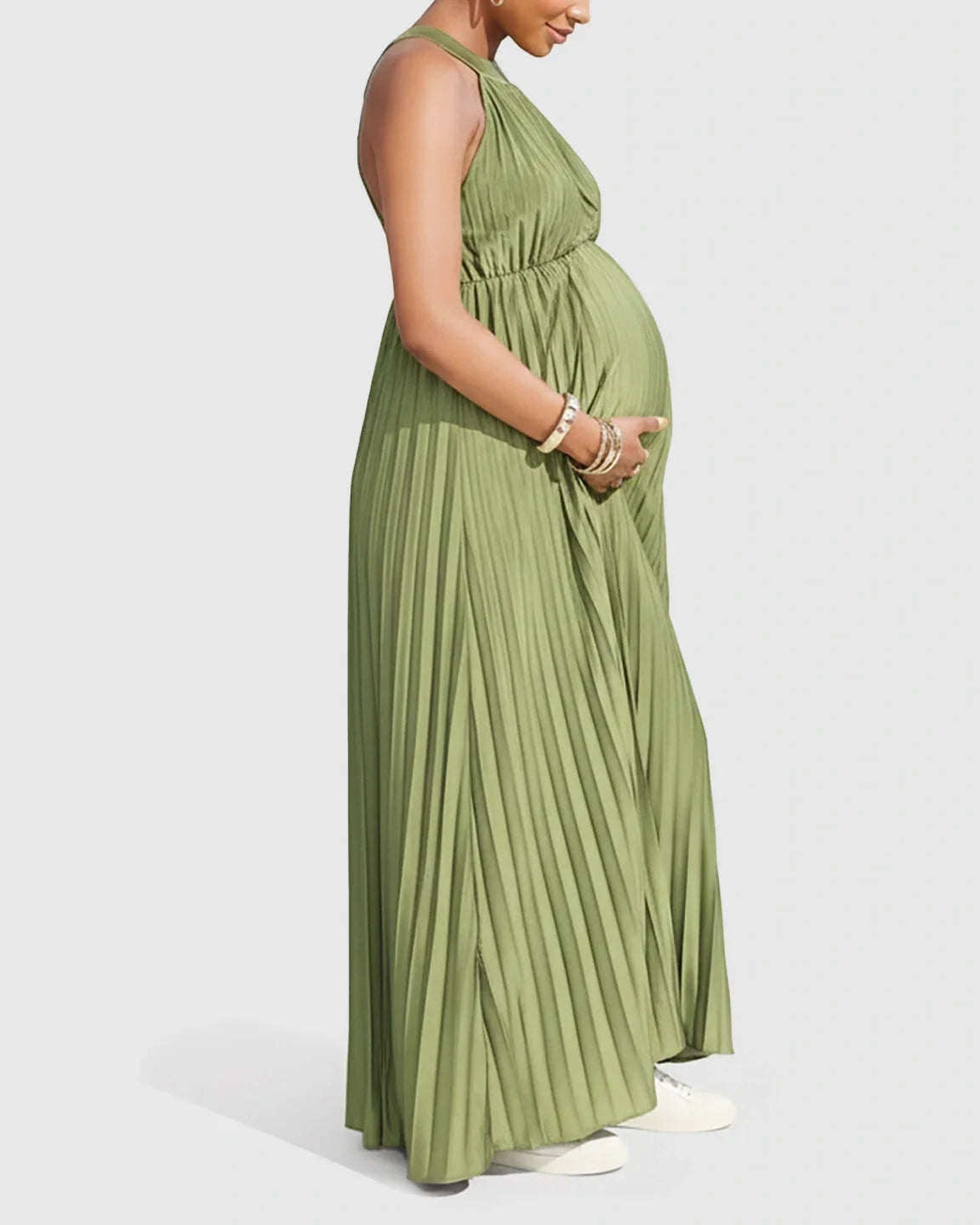 Maternity model in a green faux silk halter neck pleated maxi dress, cradling her bump.