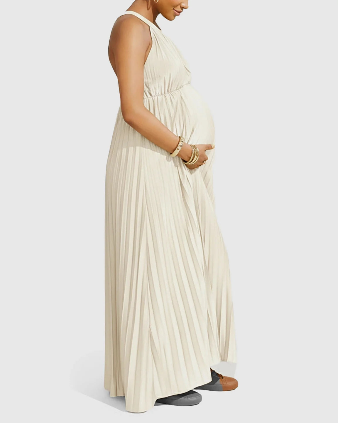 Pregnant woman in a cream faux silk pleated halter neck maternity maxi dress, side view.