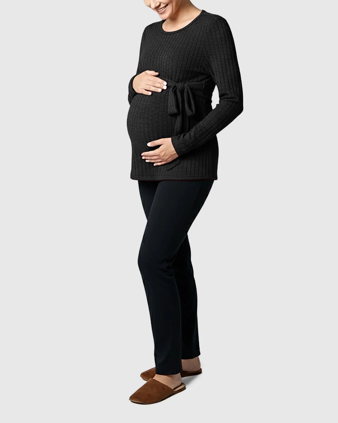 Smiling pregnant woman in a black ribbed tie-waist long sleeve maternity sweater and black pants.