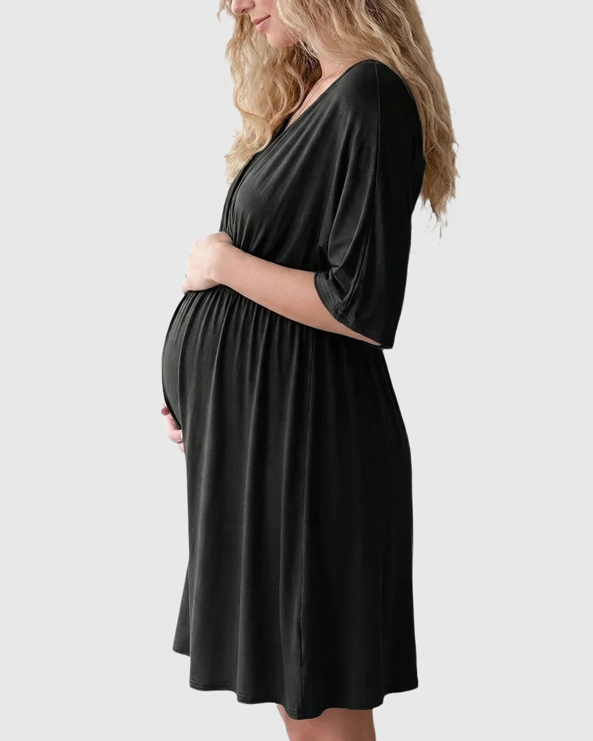Pregnant woman in a black cross-front maternity midi dress with 3/4 sleeves, flattering her bump.
