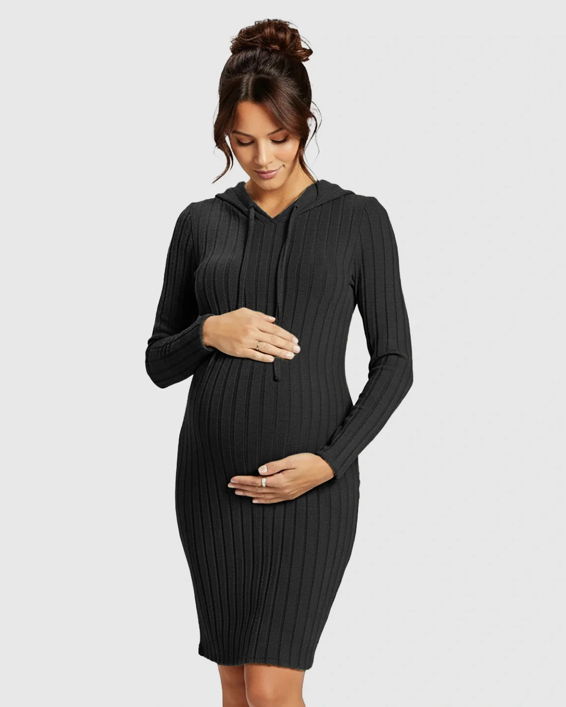 Pregnant woman in a black ribbed bodycon hooded maternity midi dress, gently holding her bump.