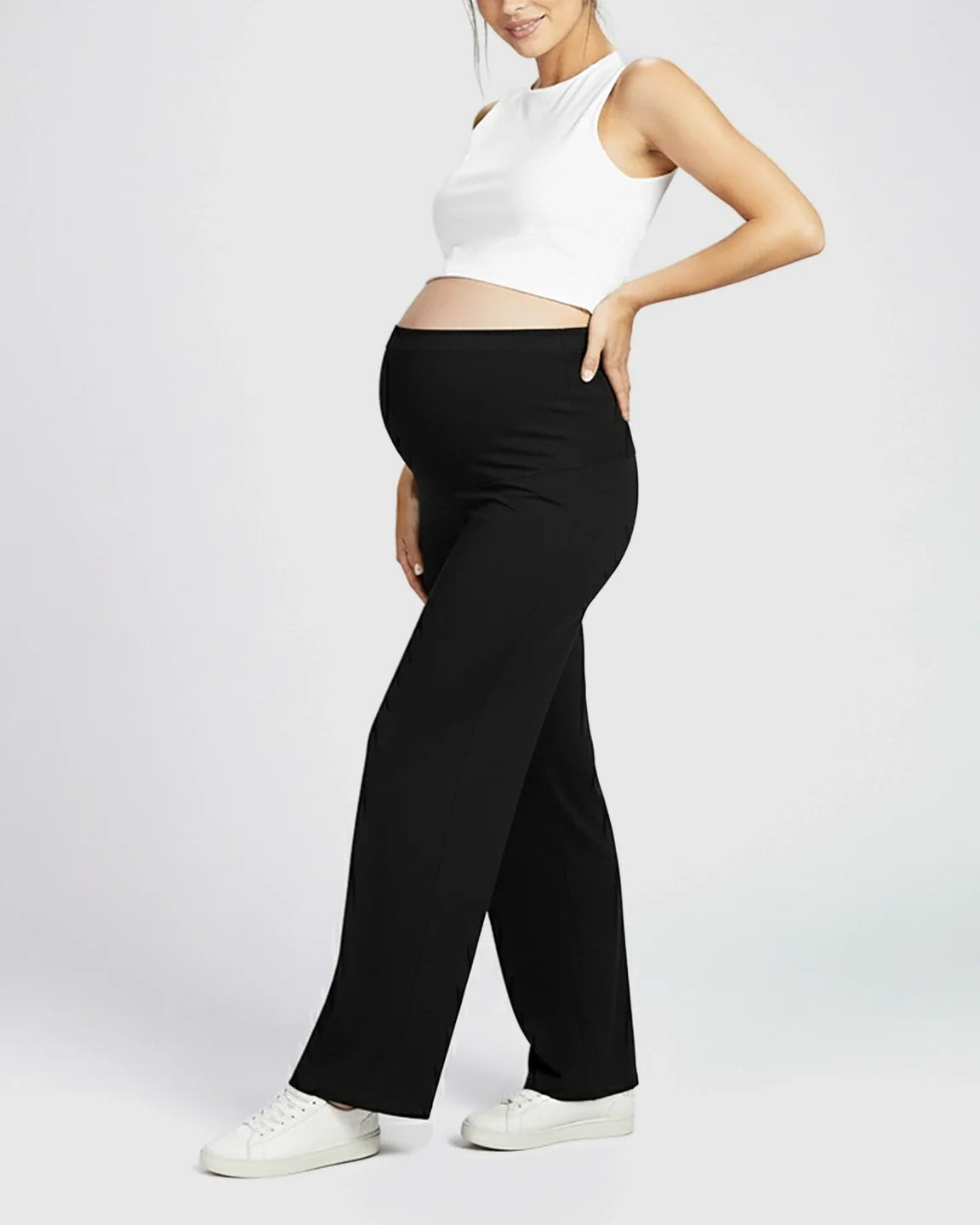 Maternity model in black Comfort Fit elastic waist pants, white crop top, and sneakers.