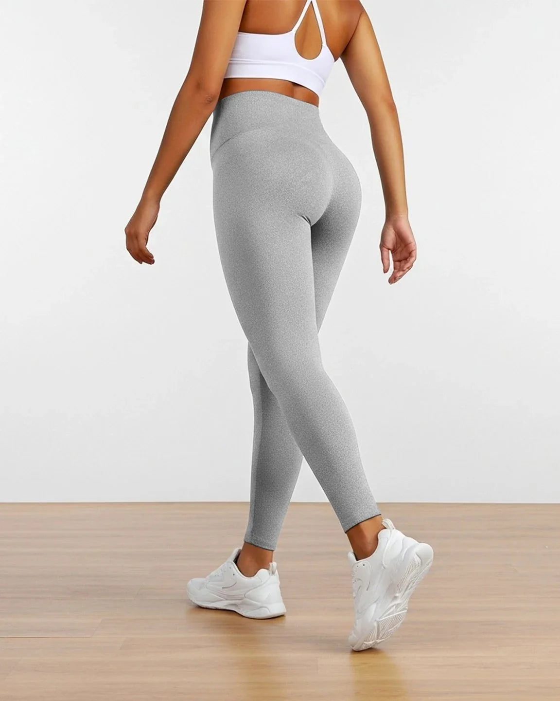 Woman from behind wearing light grey sculpting ankle-length maternity leggings and a white sports bra.