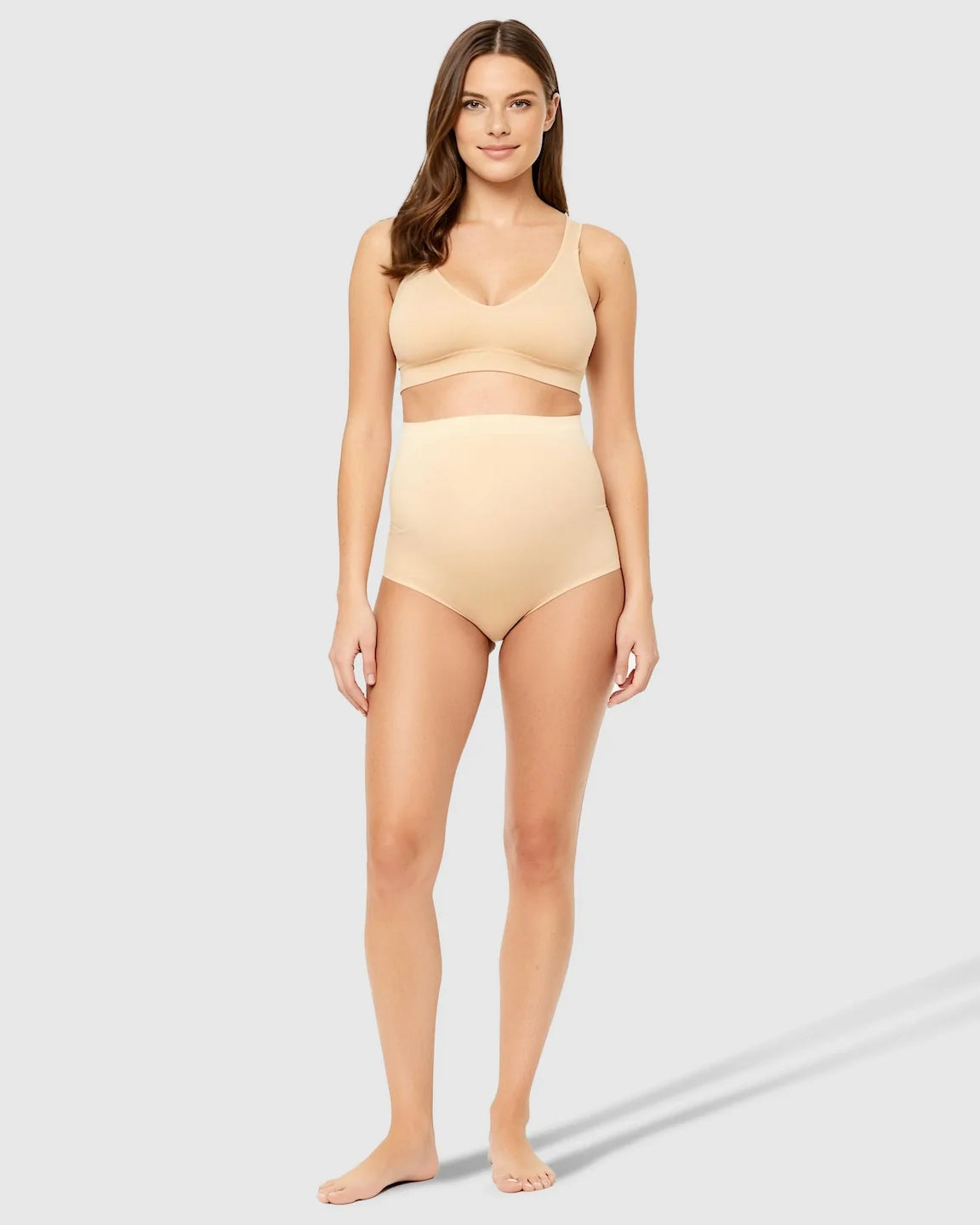 Woman in nude high-waist seamless belly-support maternity underwear and matching bra.