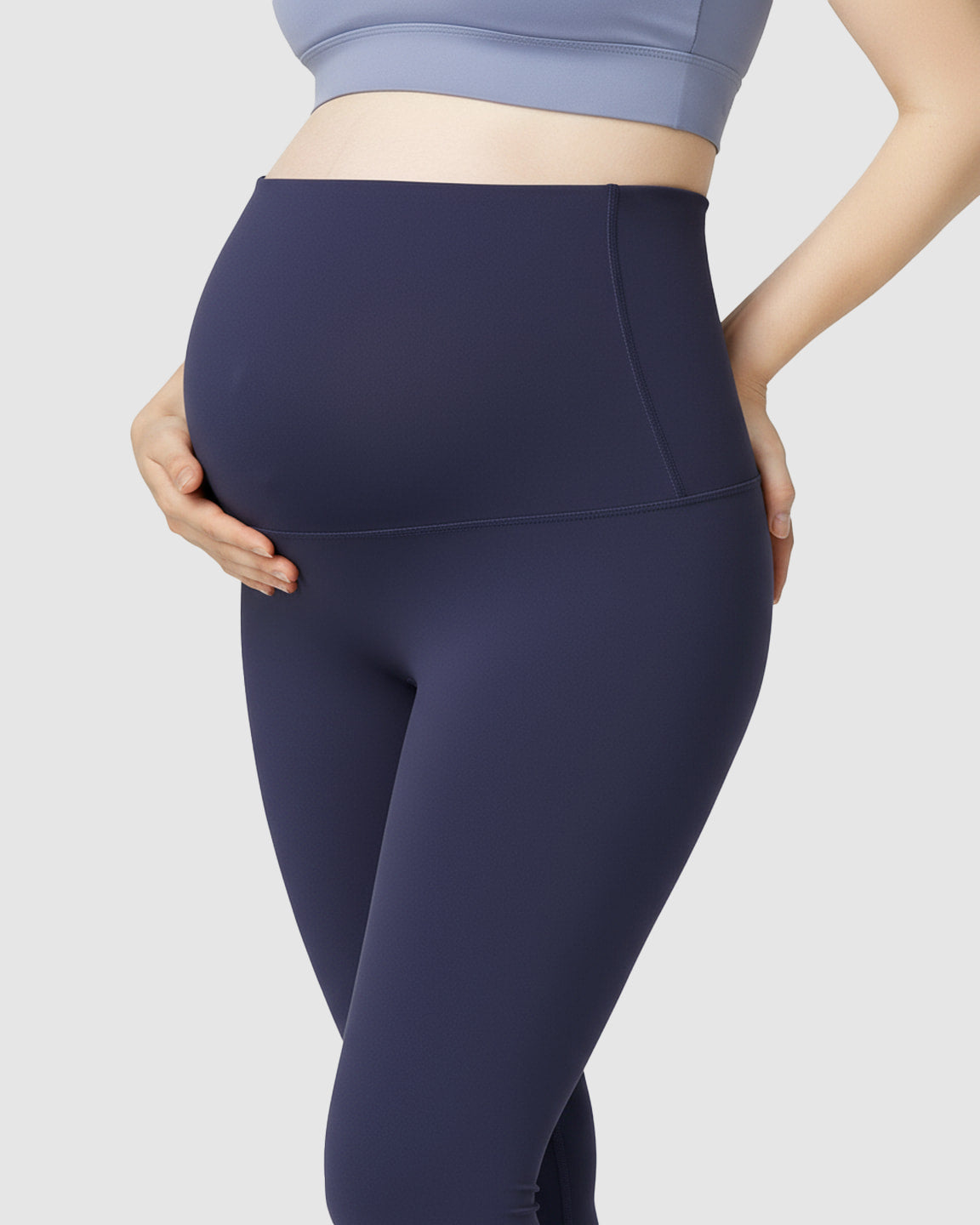 Pregnant woman wearing navy blue high-waist soft stretch maternity leggings, supporting her bump.