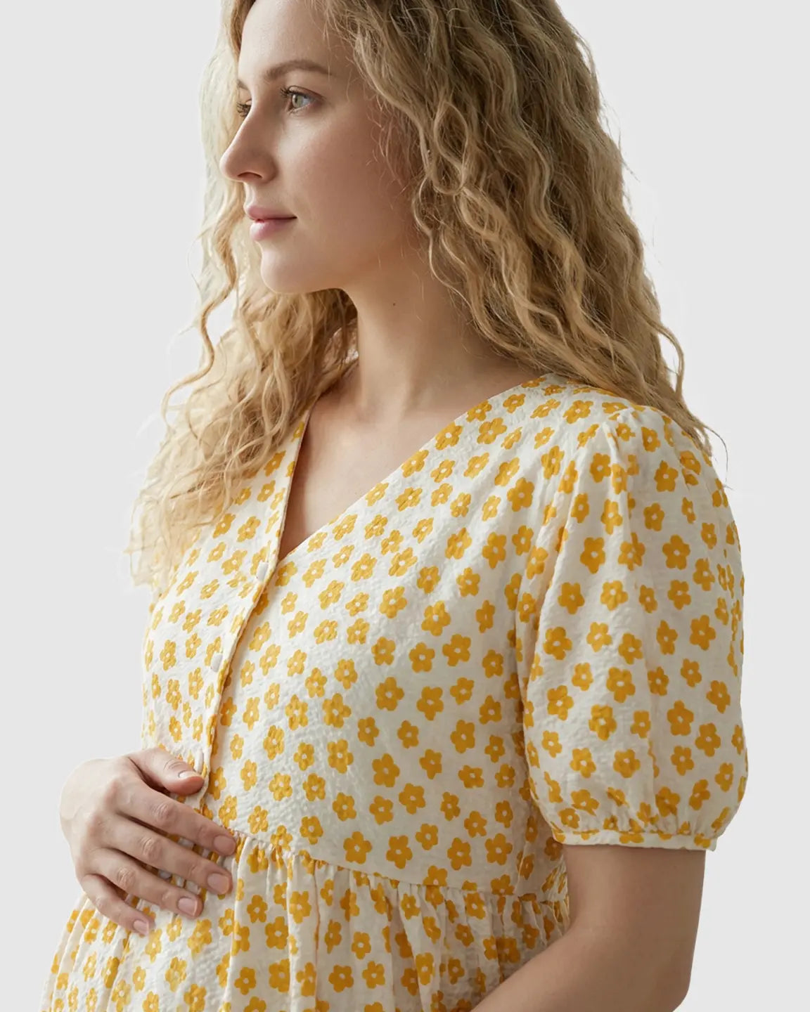 Blonde woman in a white and yellow floral print maternity nursing dress with a V-neck and button-front.