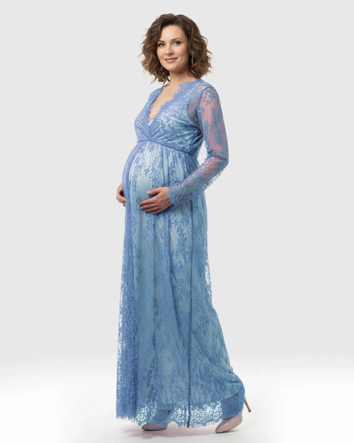 Maternity maxi dress in sheer floral blue lace with empire waist and long sleeves, worn by a pregnant woman.