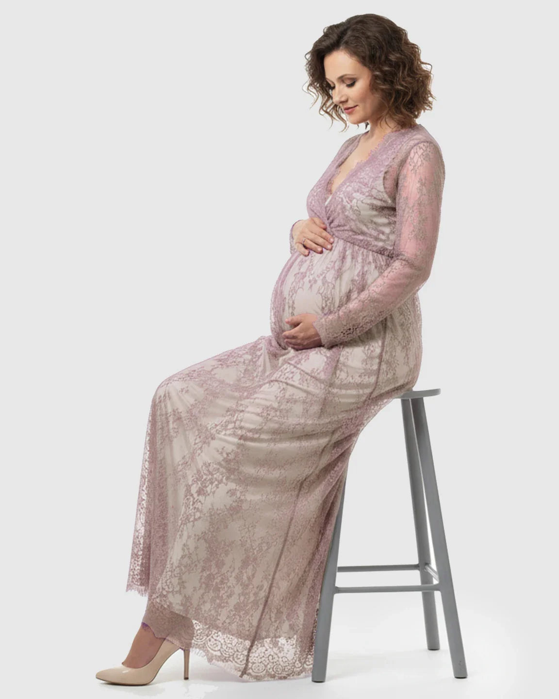 Pregnant woman in a sheer floral lace empire waist maternity maxi dress, light pink, sitting.