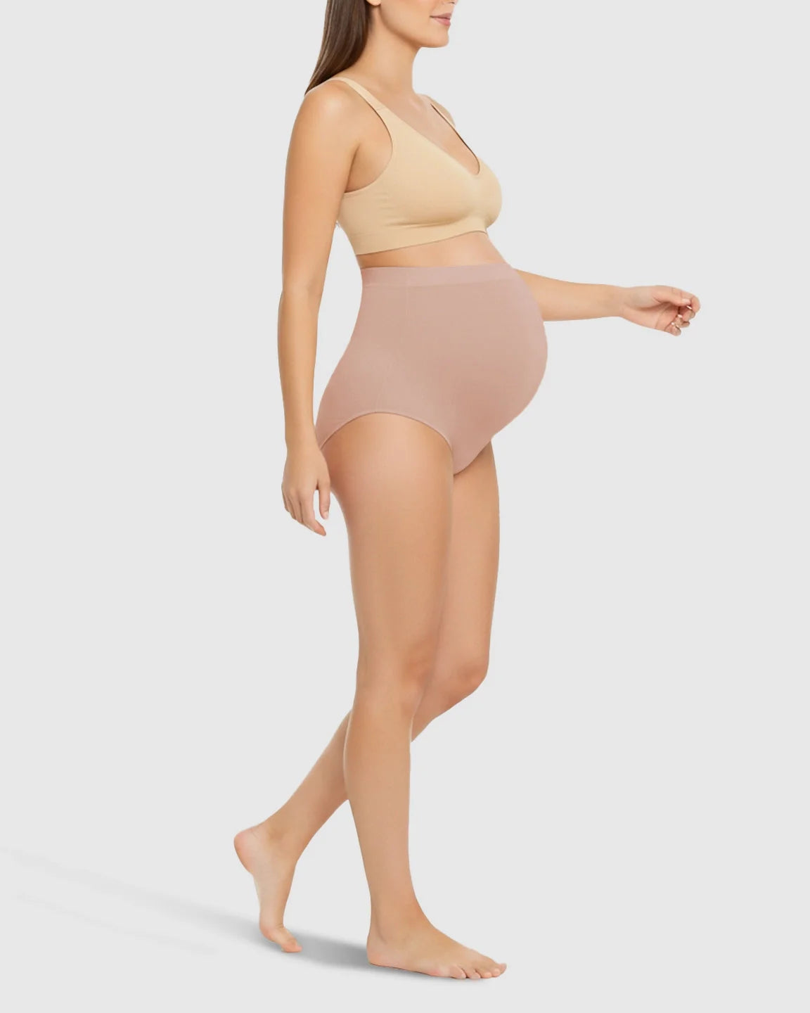 Pregnant woman wearing nude high-waist seamless belly-support maternity underwear and a matching bra.