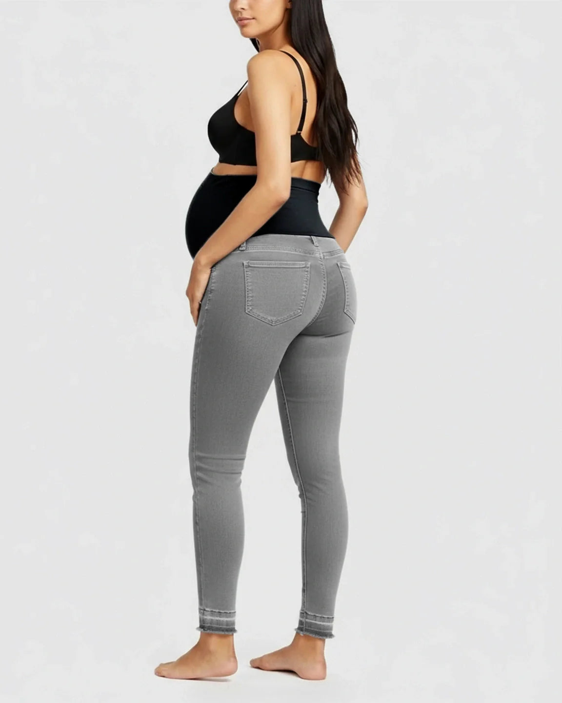 Maternity model wearing gray high-waist skinny jeans with a black elastic belly band and raw hem.