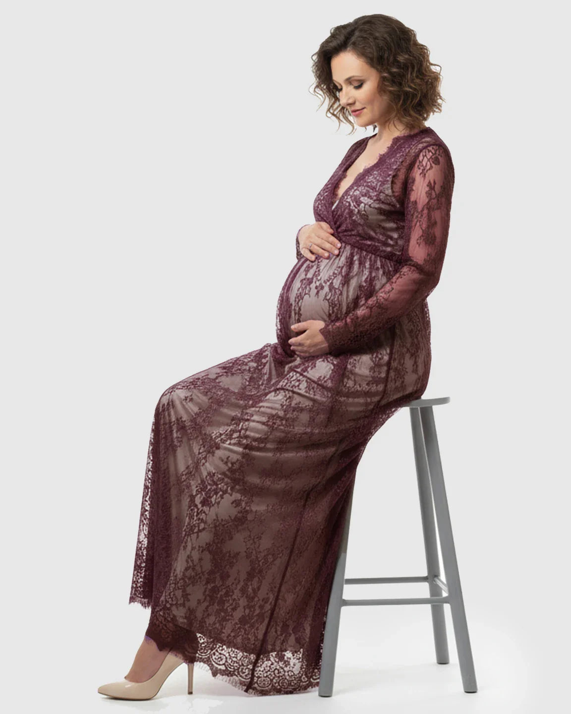 Pregnant woman in a plum sheer floral lace empire waist maternity maxi dress, holding her bump.
