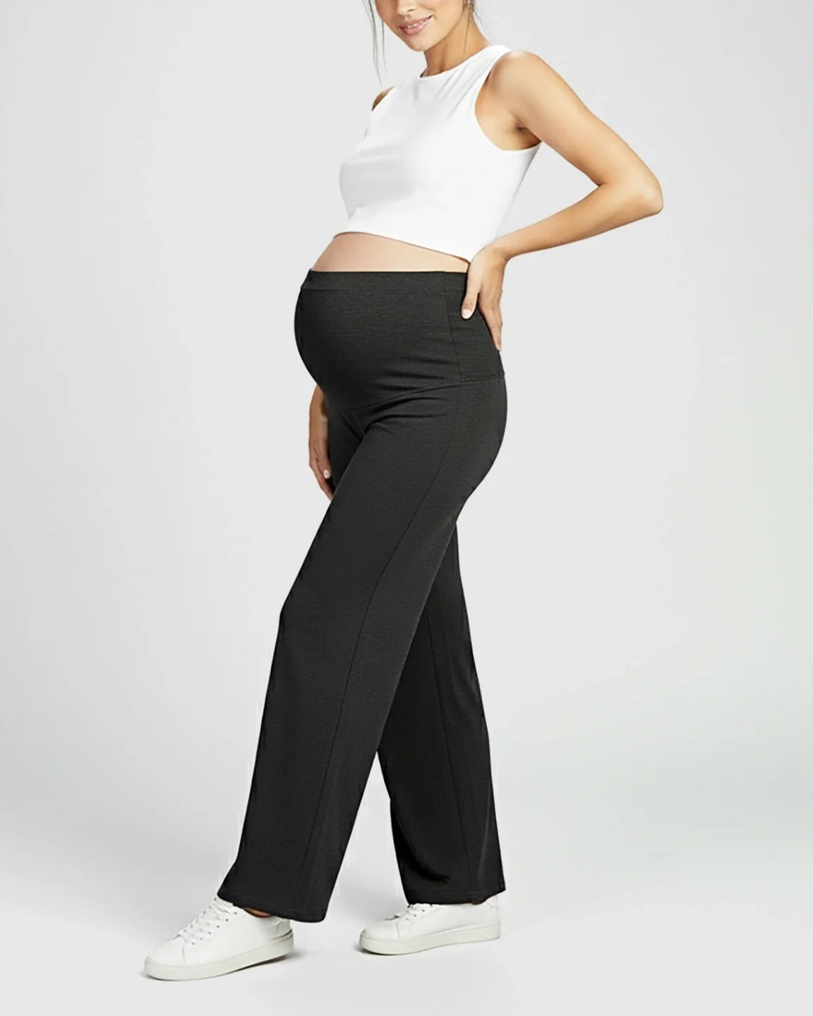 Maternity model in black Comfort Fit elastic waist pants, white crop top, and sneakers.