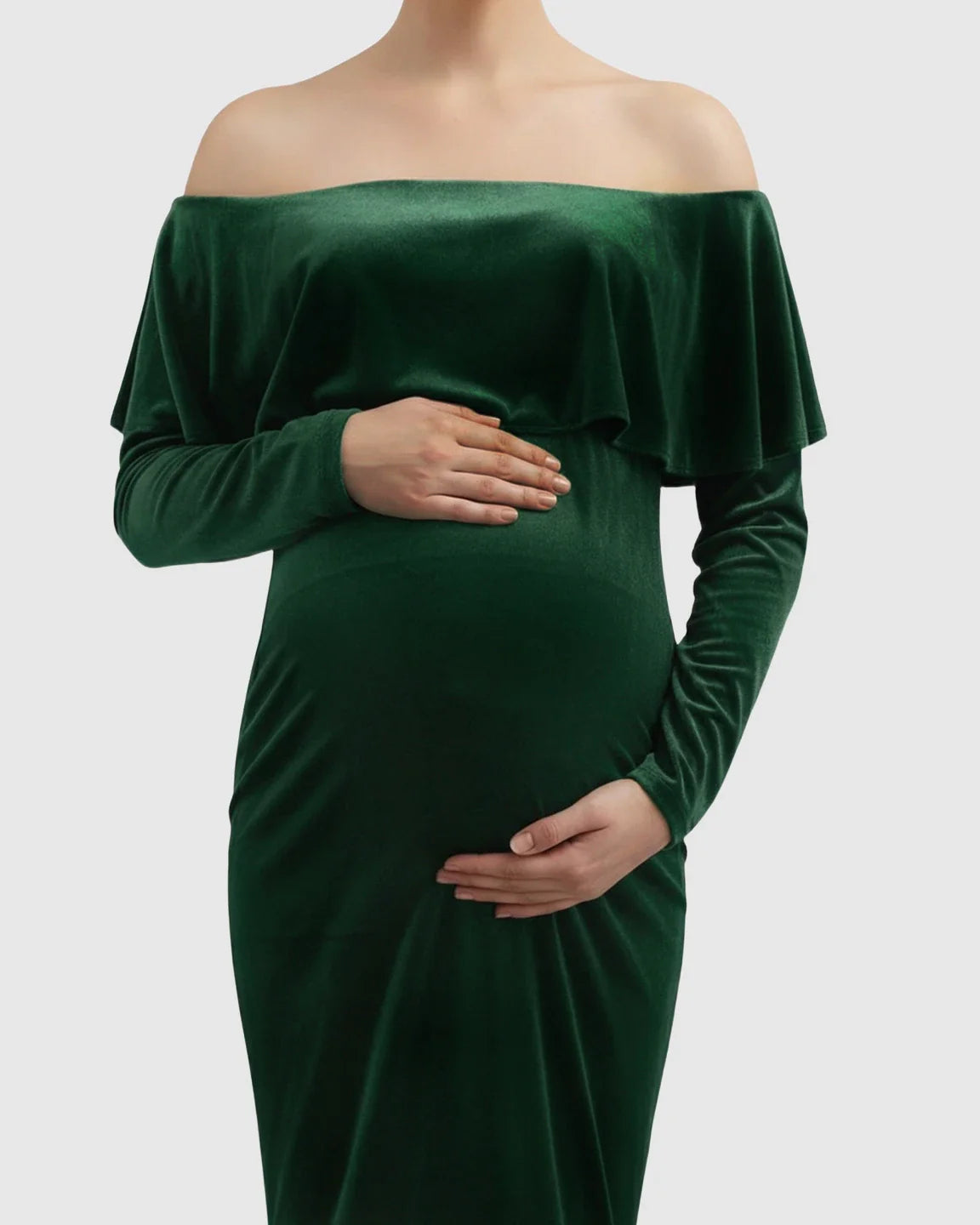 Emerald green velvet off-shoulder maternity gown with long sleeves, fitted bodice, and flowing skirt, highlighting a pregnant belly.