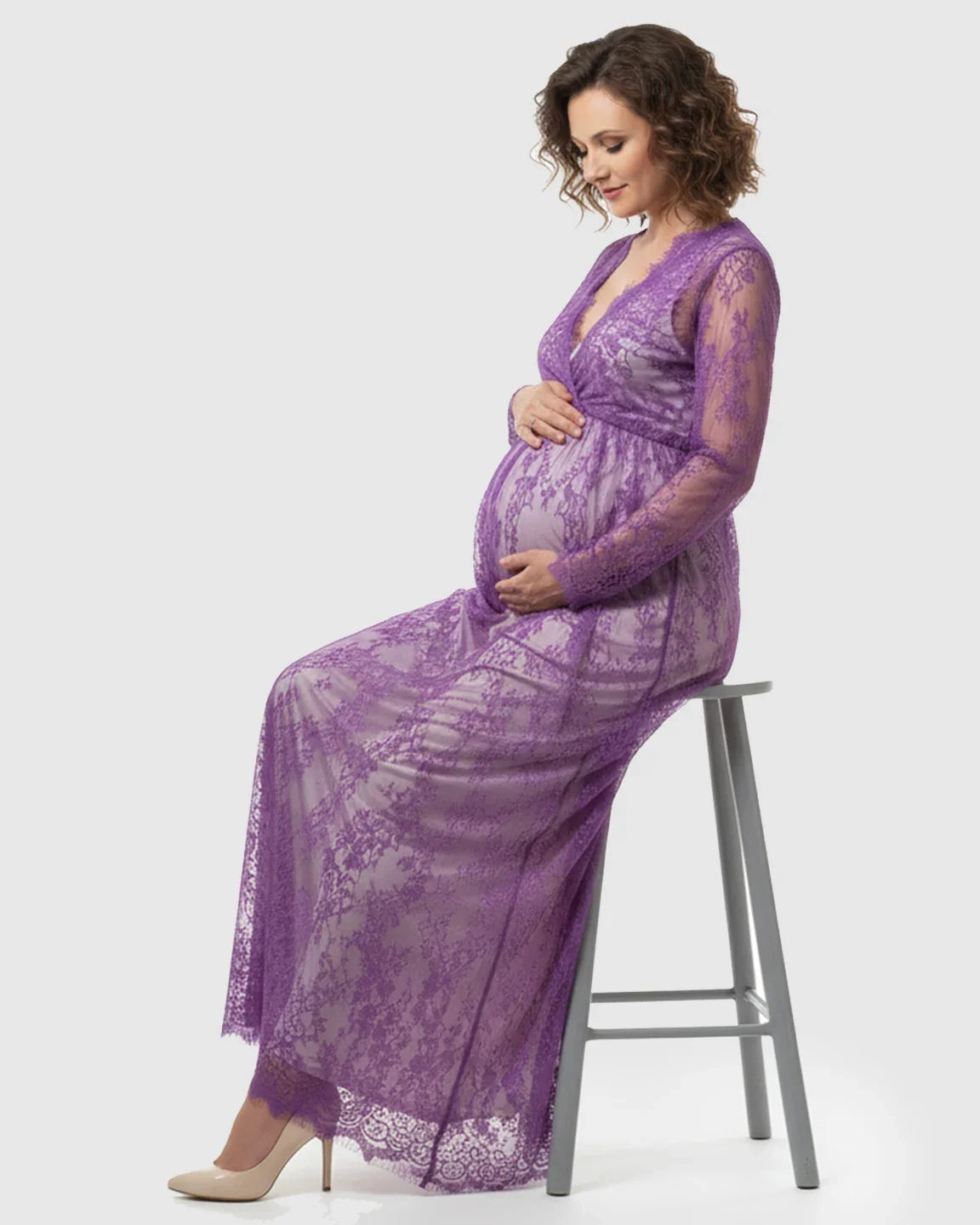 Maternity maxi dress in sheer purple floral lace, empire waist, V-neck, long sleeves, worn by a pregnant woman.