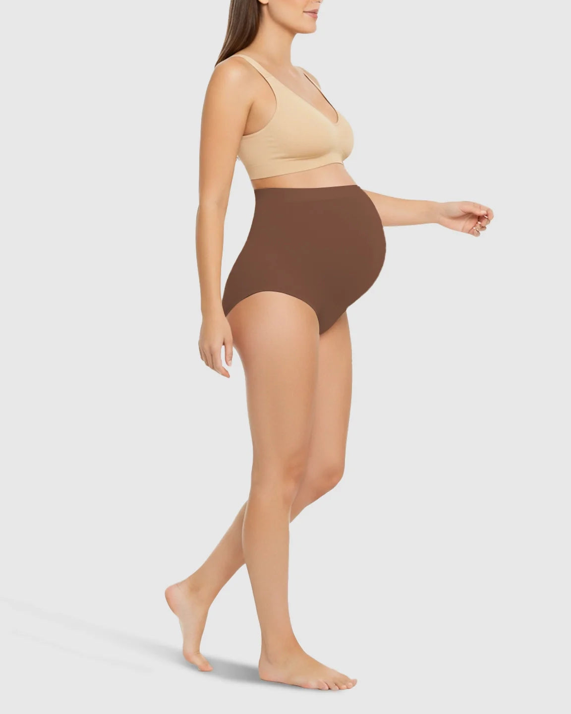 Pregnant woman wearing brown high-waist seamless belly-support maternity underwear and a beige bra.
