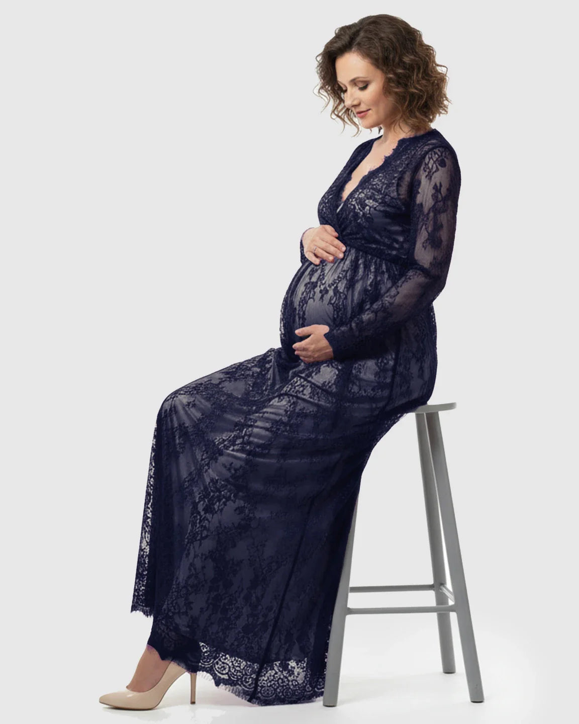 Pregnant woman in a navy sheer floral lace empire waist maternity maxi dress, holding her bump.