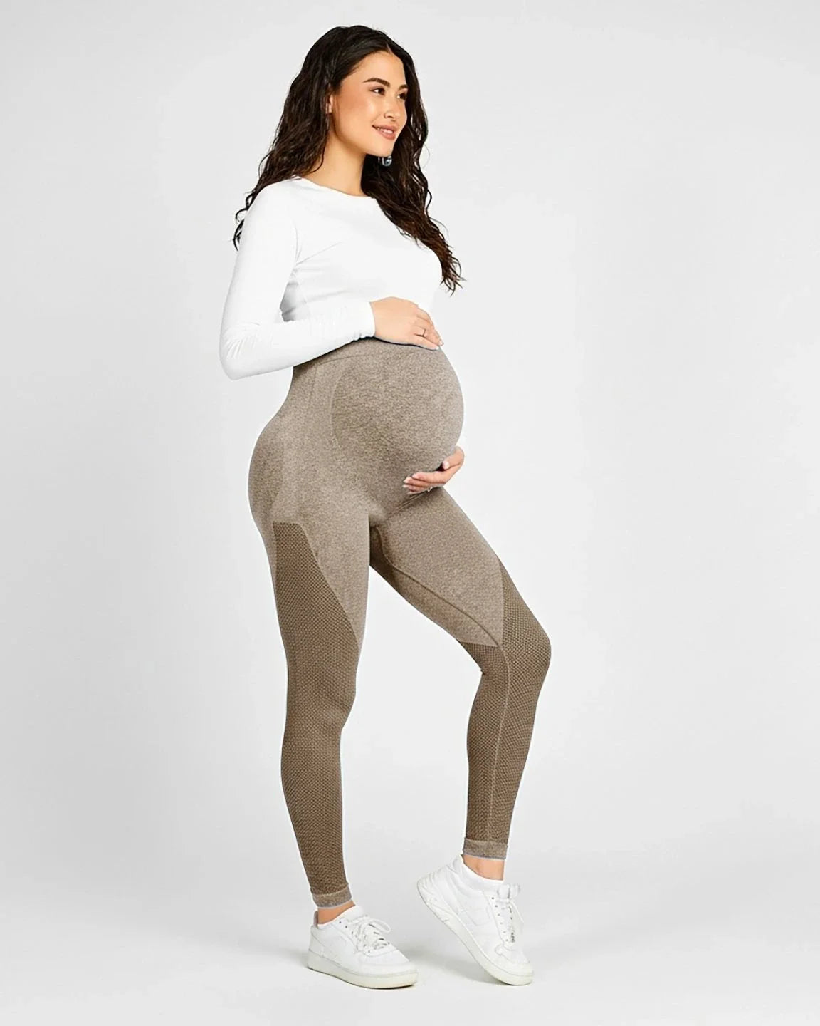 Smiling pregnant woman in high-waisted, body-hugging brown maternity leggings with textured panels.