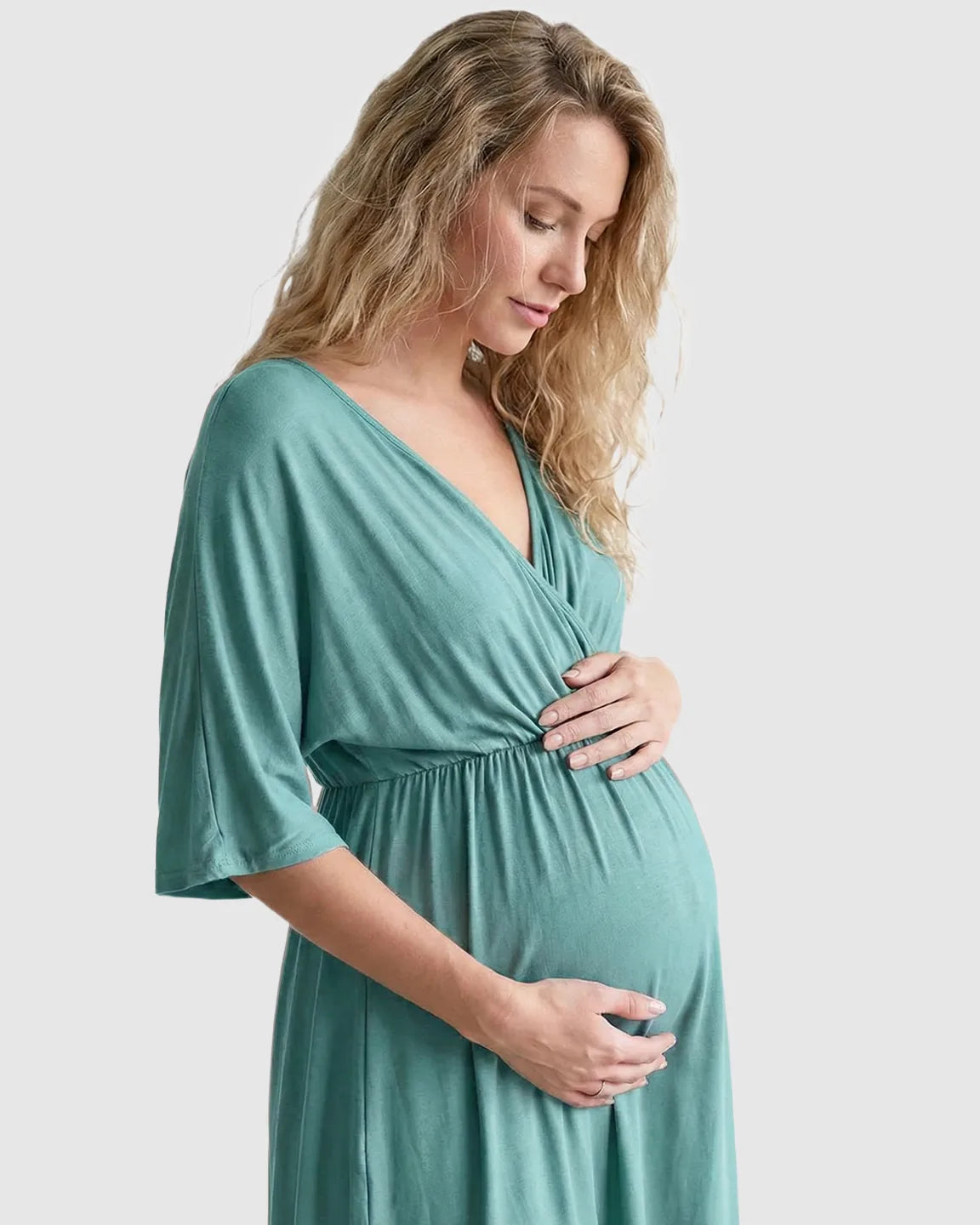 Pregnant woman in a teal cross-front maternity midi dress with 3/4 sleeves, flattering her bump.