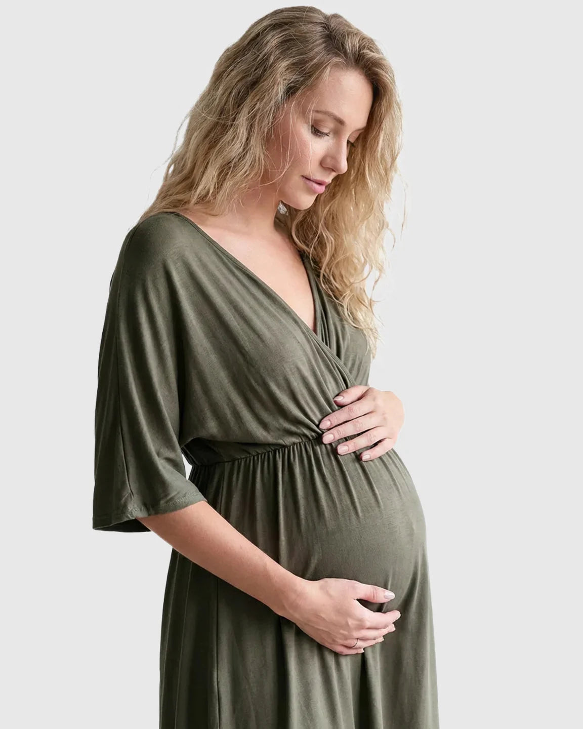 Blonde pregnant woman in a soft olive green cross-front maternity midi dress with 3/4 sleeves.