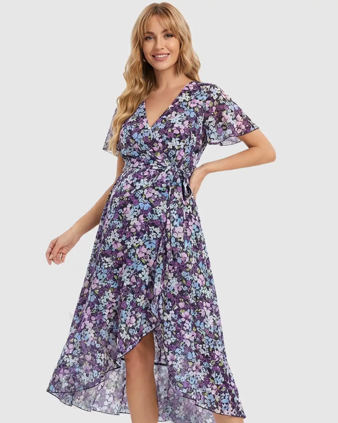Smiling pregnant woman in a purple floral V-neck maternity midi dress with ruffled hem and tie waist.