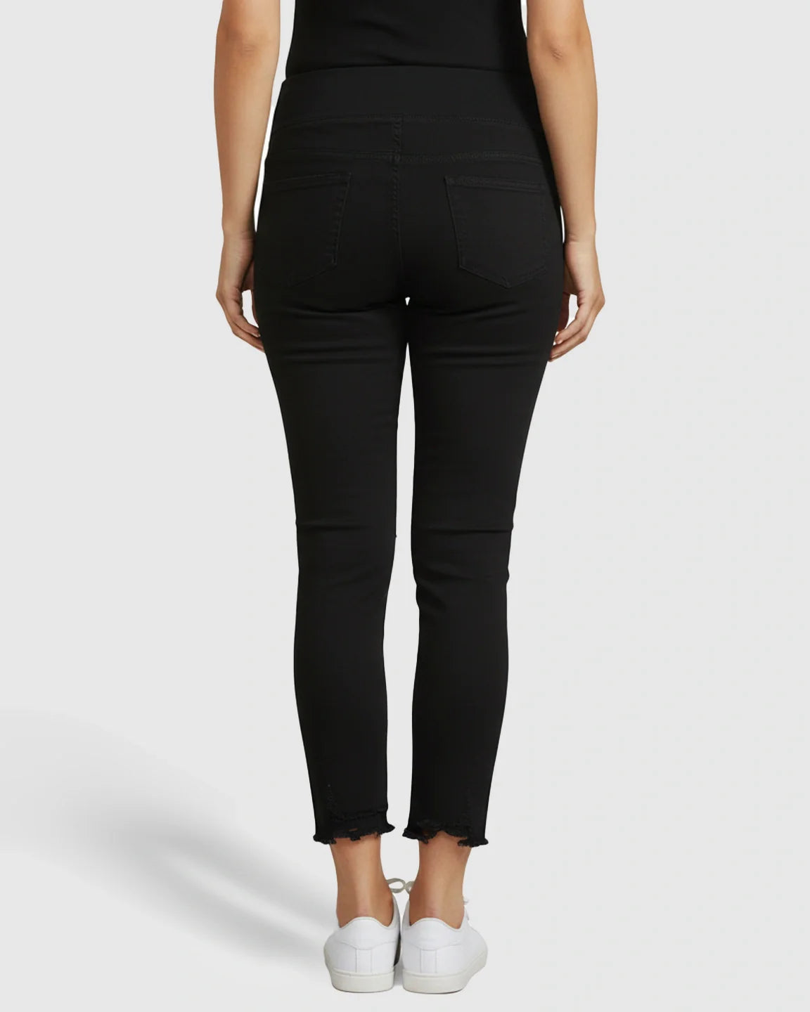 Back view of black maternity skinny jeans with over-belly support panel and ankle-fray hem.