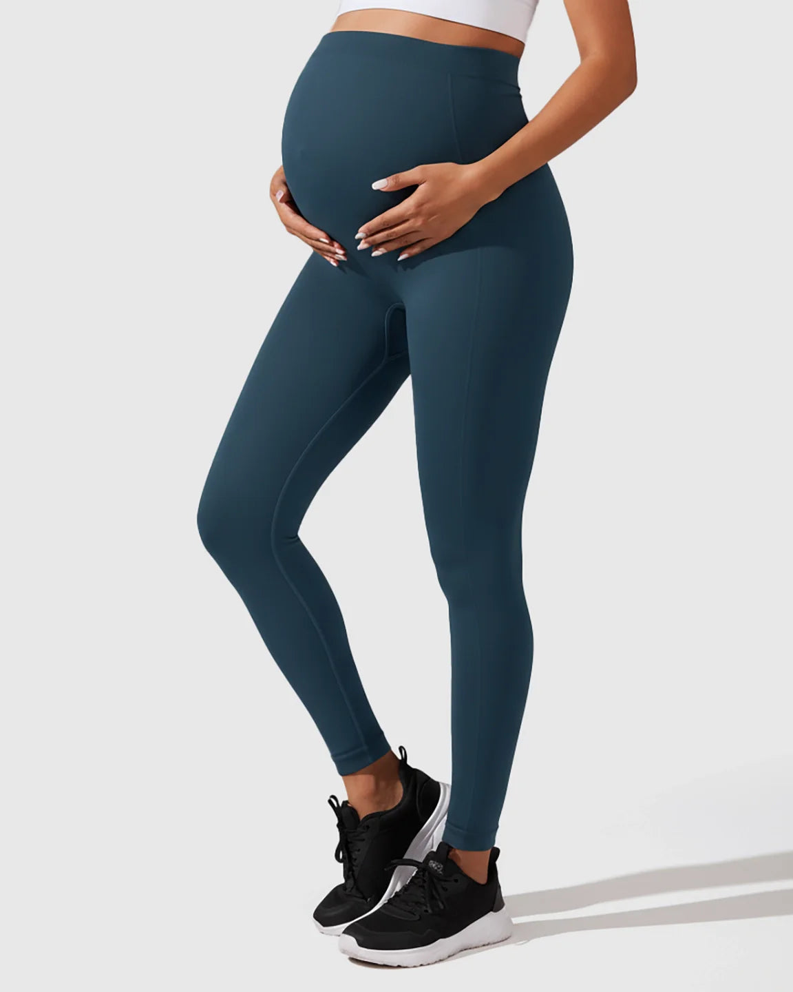 Maternity model wearing seamless, high-waisted teal leggings with full-belly support and a sleek, sculpting fit.