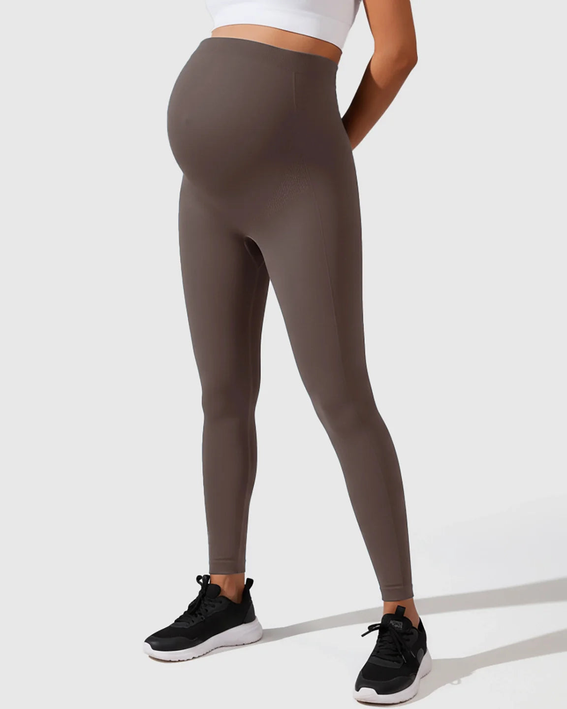 Seamless, high-waisted M-shape maternity leggings in a dark taupe color, worn by a pregnant woman.