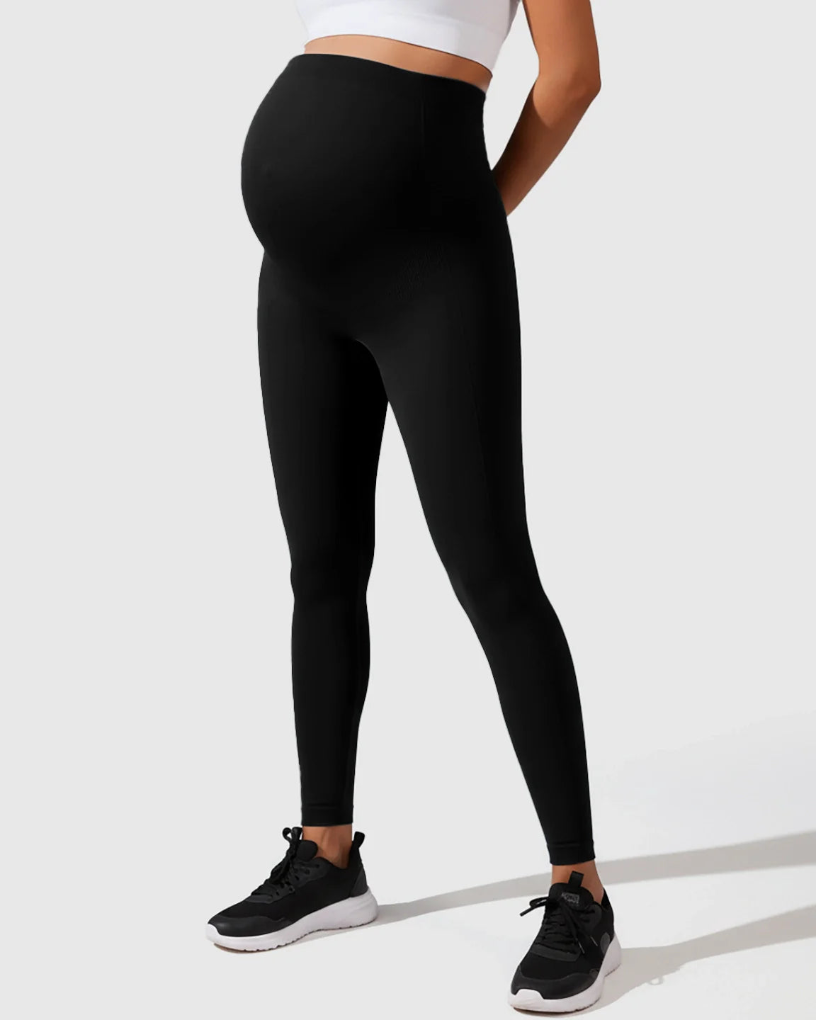Black seamless M-shape maternity leggings with full-belly support, worn by a pregnant woman.