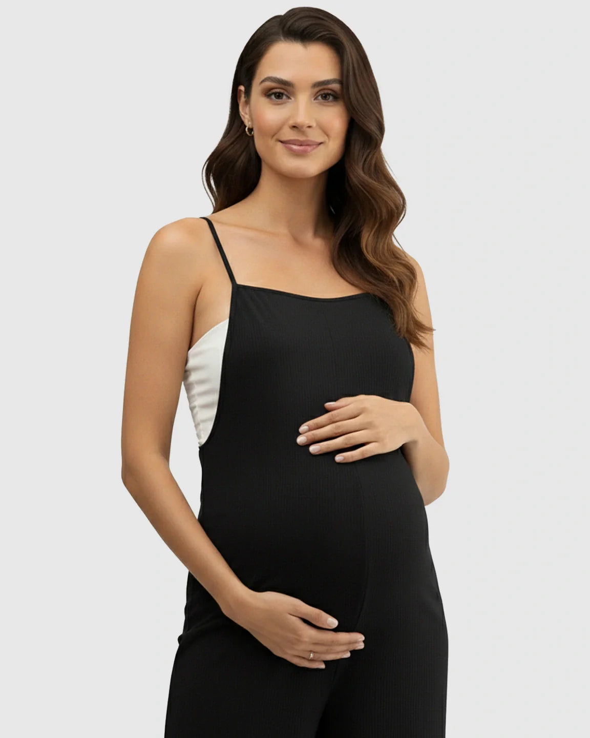 Pregnant woman models a black ribbed spaghetti strap wide-leg maternity jumpsuit with a white top underneath.