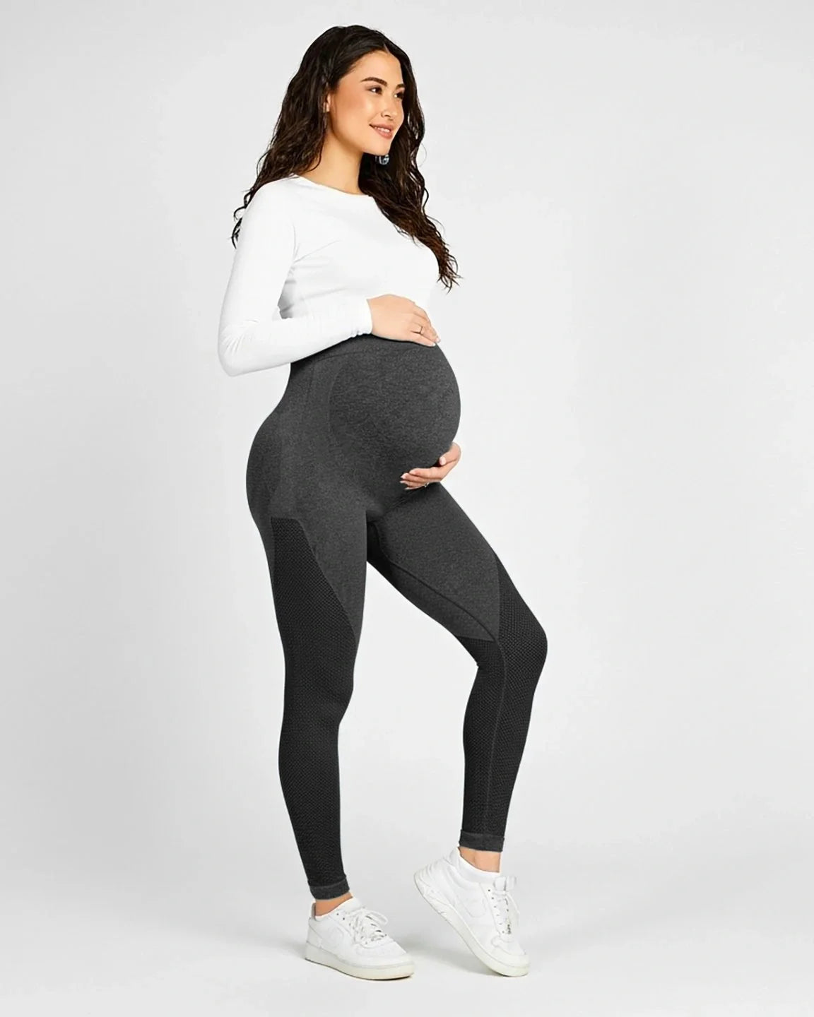 Pregnant woman in dark grey high-elastic, body-hugging maternity leggings with textured details, cradling her bump.
