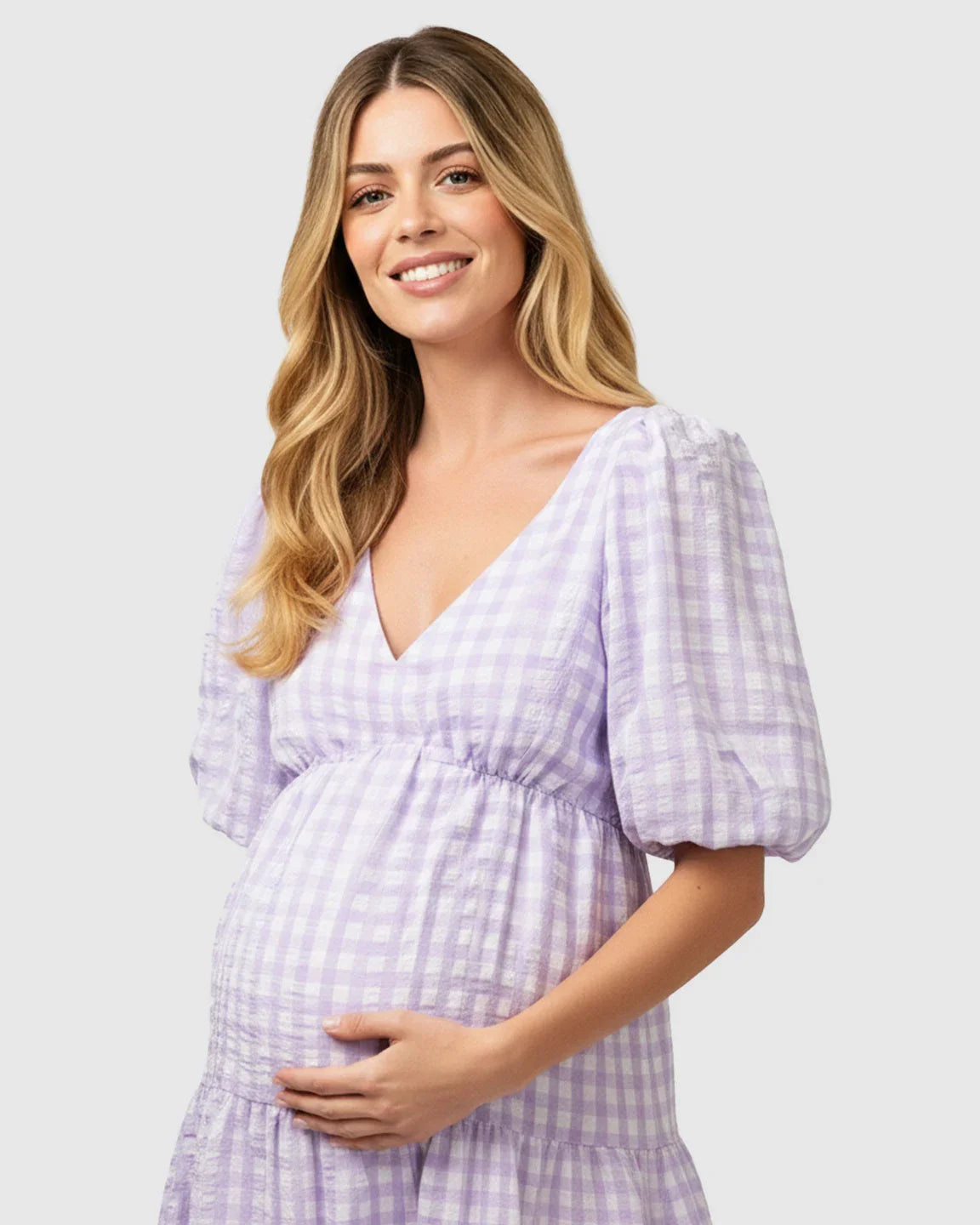Smiling pregnant woman in a lavender and white checkered maternity maxi dress with puffed sleeves.