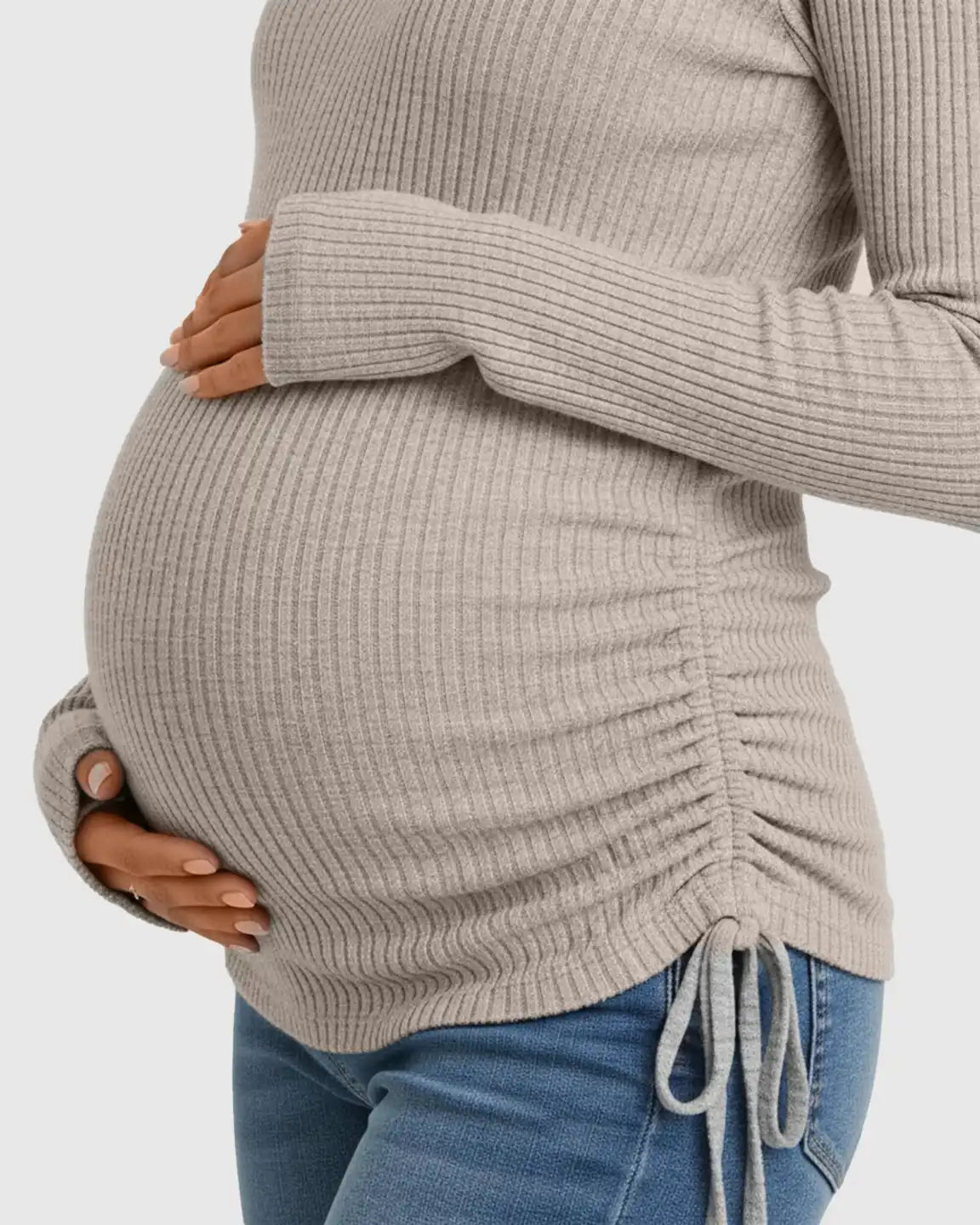 Pregnant woman in a beige ribbed long-sleeve maternity top with adjustable side drawstrings, paired with jeans.