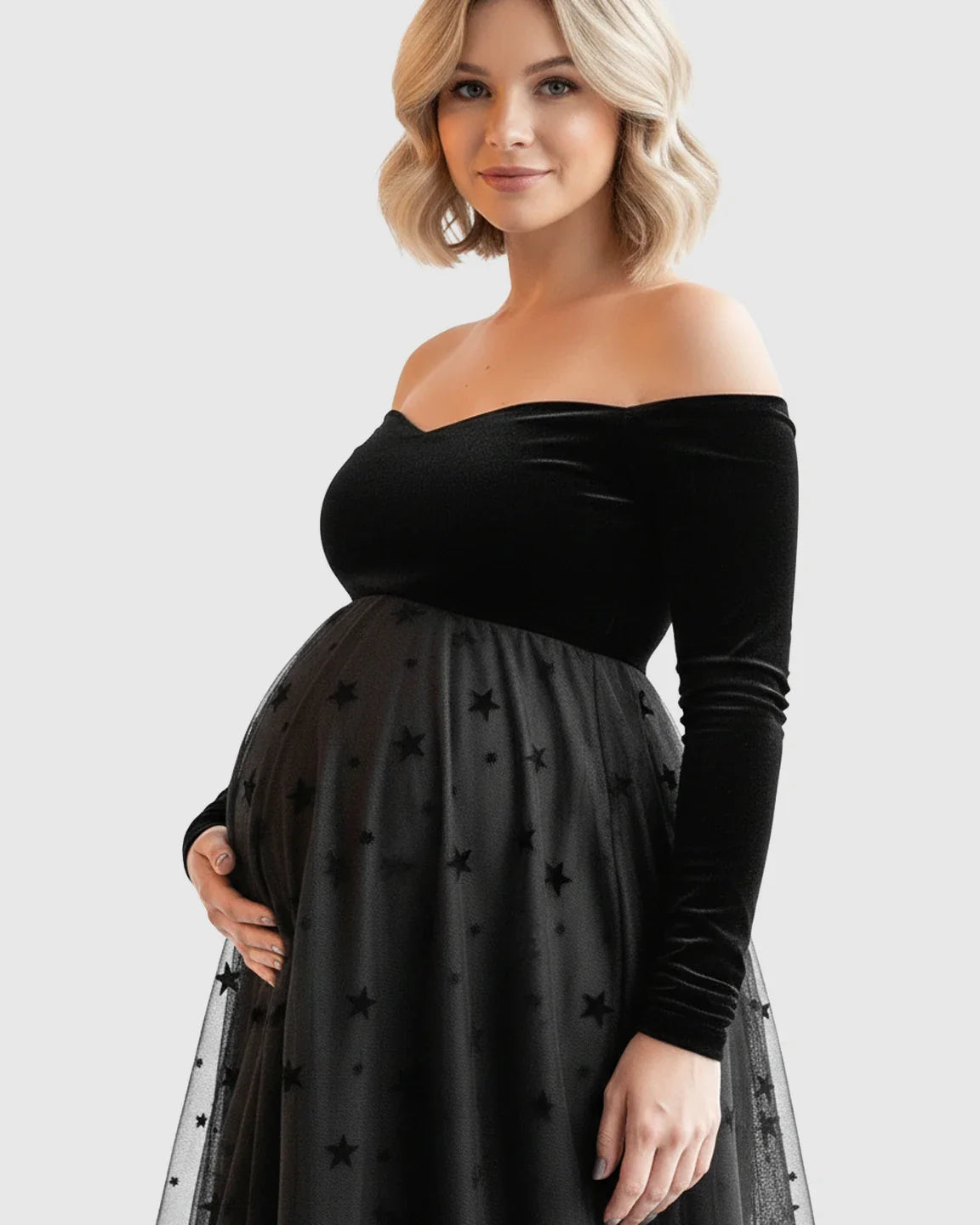 Pregnant woman in black off-shoulder velvet and star-flocked mesh maternity midi dress.