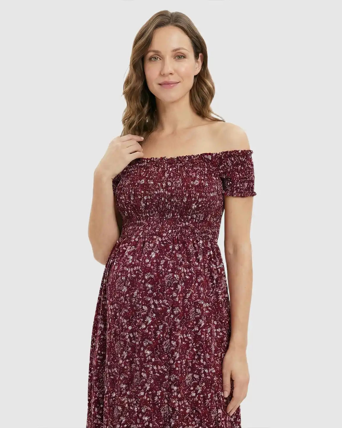 Pregnant woman in a red floral off-shoulder maternity maxi dress with a side slit.