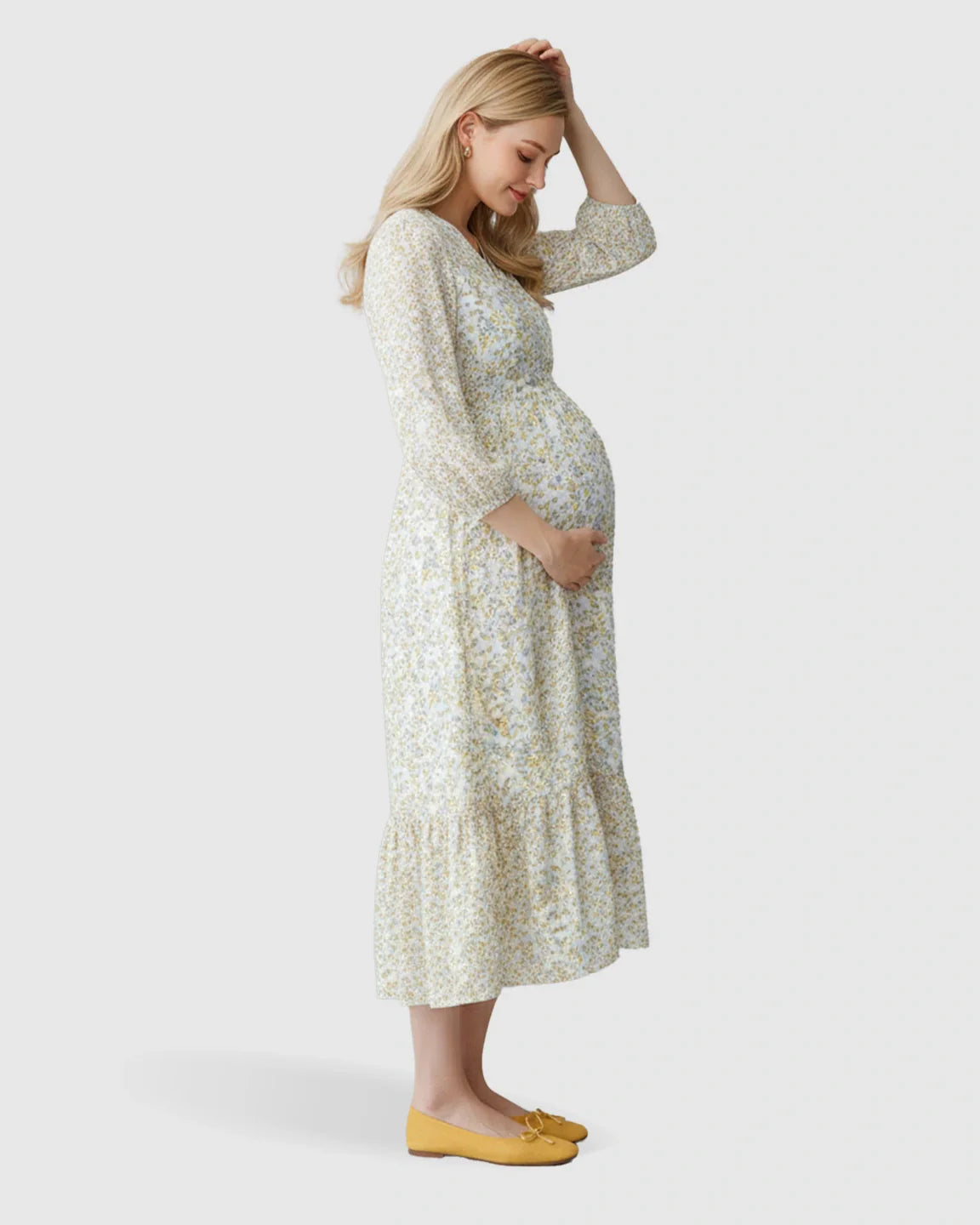 Pregnant woman in a white floral ruffle hem smocked waist maternity midi dress with yellow flats.