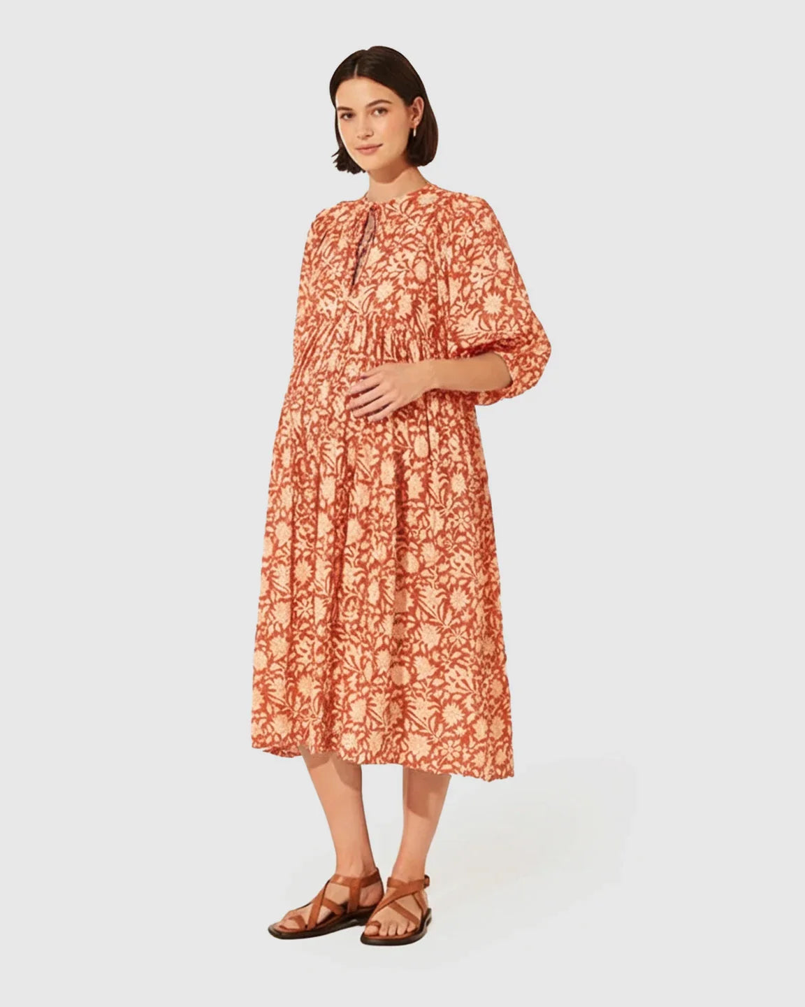 Pregnant woman in a rust and cream floral maternity midi dress with gathered shoulders, puff sleeves, and knot detail.