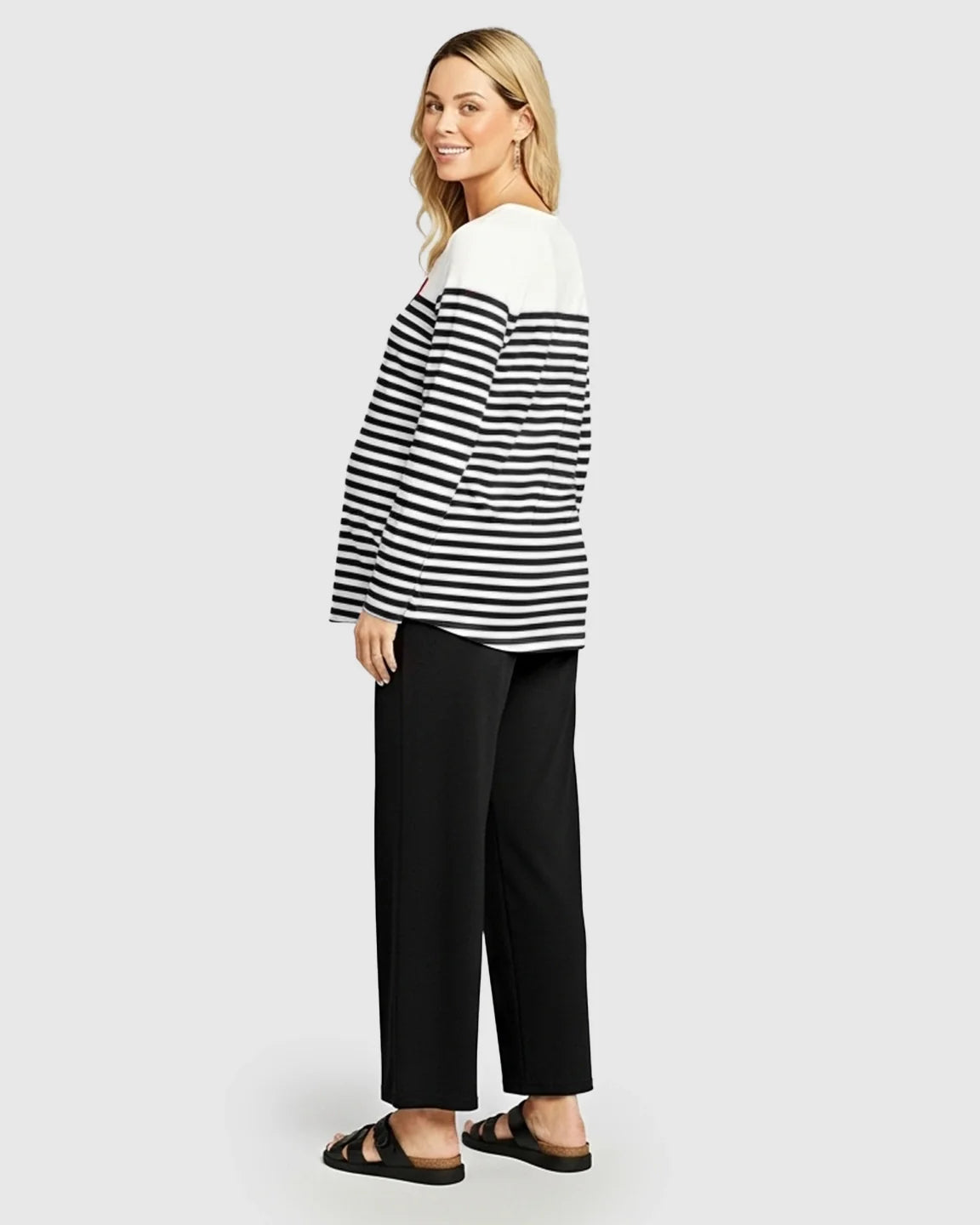 Smiling pregnant woman in a black and white striped loose-fit maternity top with a red heart and black pants.