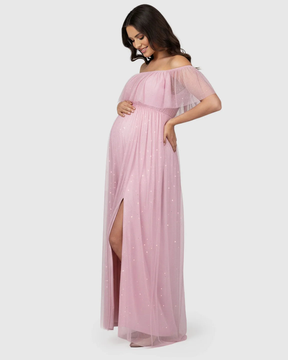 Smiling pregnant woman in a pink off-shoulder mesh slit maternity gown with glitter details.