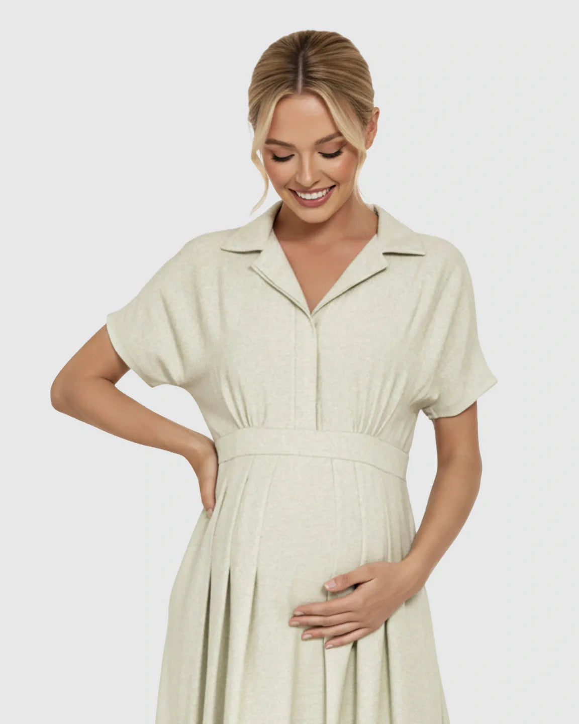 Smiling pregnant woman in a light green lapel collar A-line maternity midi dress, holding her bump.