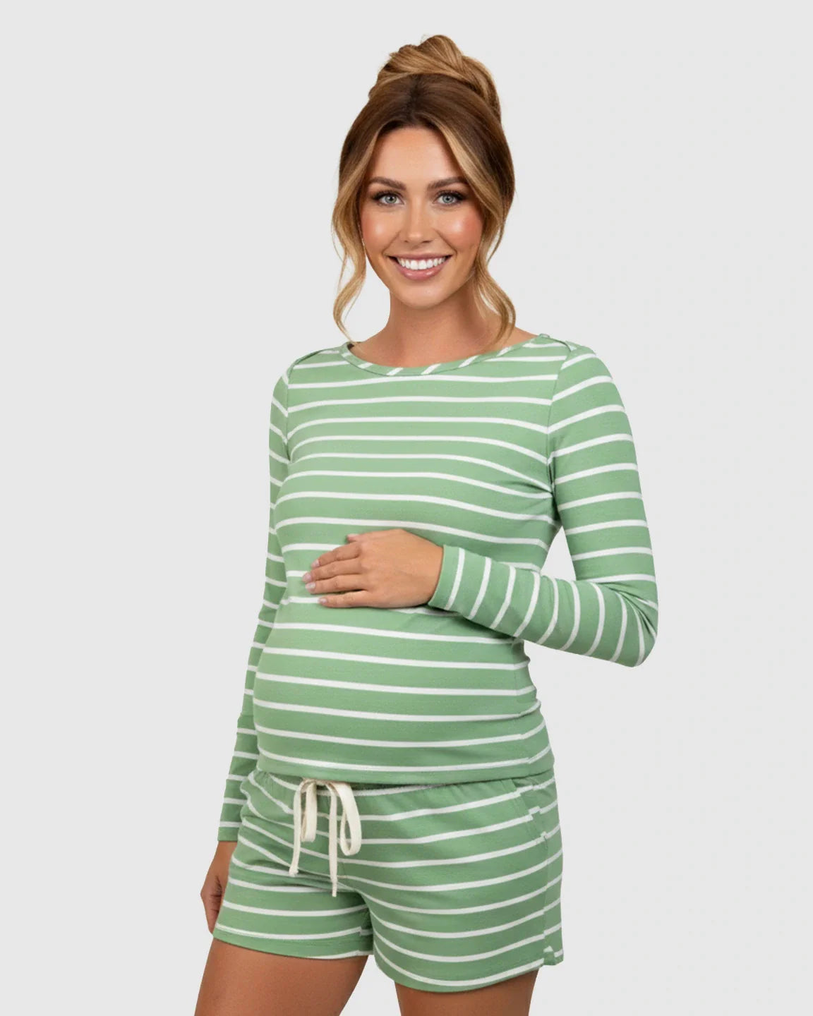 Smiling pregnant woman in a green and white striped long-sleeve maternity lounge top and drawstring shorts.